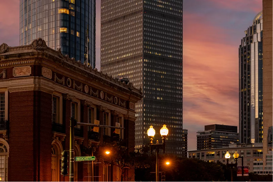 Cityscape at dusk with historic and modern buildings under sunset sky.