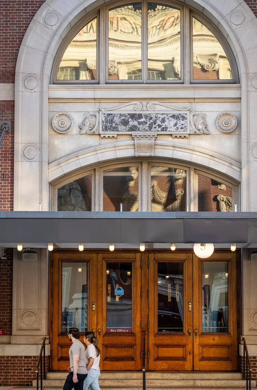 Ornate theater entrance with wooden doors and two people walking past.