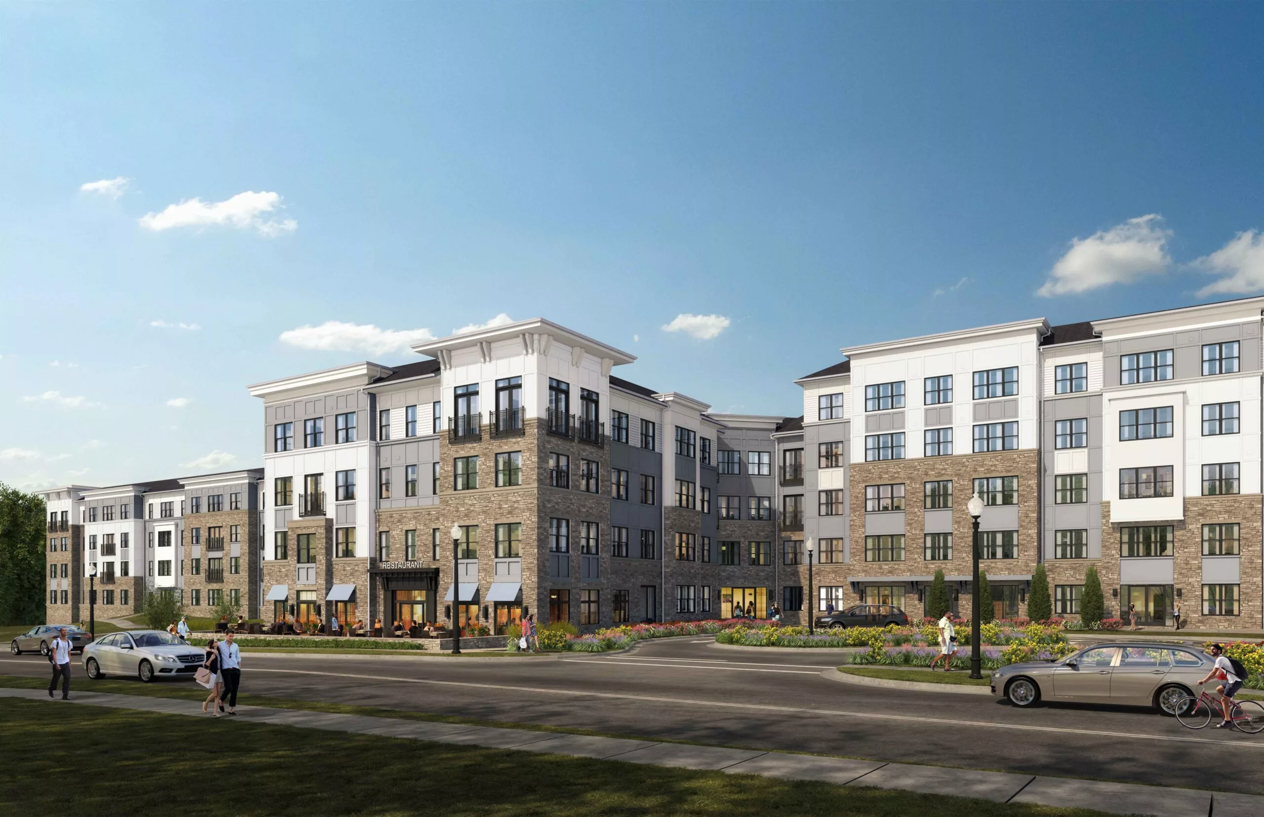Daytime view of a four-story suburban apartment building with a mix of white and tan stone exterior, featuring retail space at the ground level and landscaped surroundings.