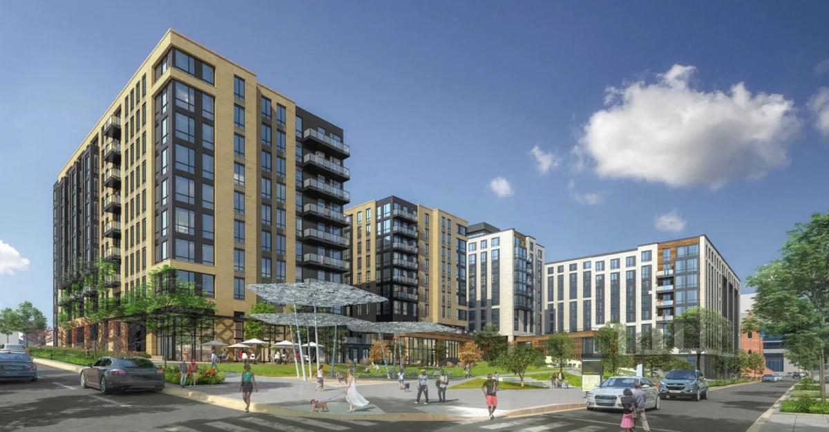 Contemporary multi-building residential complex with tan and black facades, surrounding a landscaped public plaza with people walking and sitting.