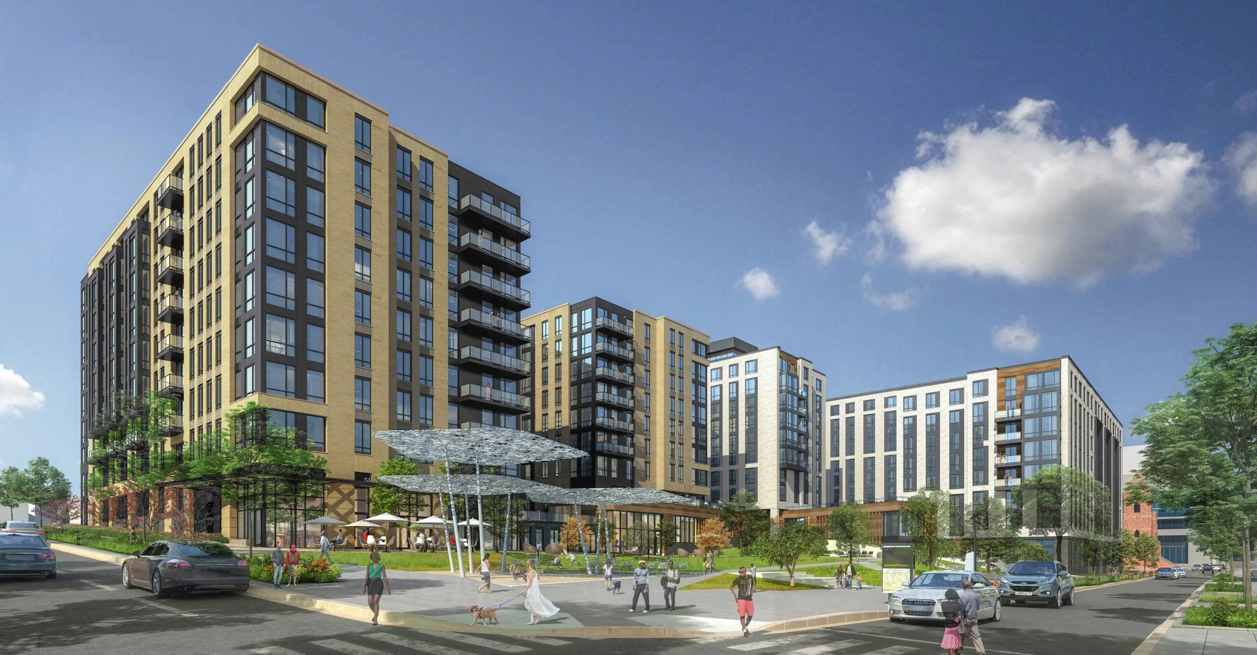 Contemporary multi-building residential complex with tan and black facades, surrounding a landscaped public plaza with people walking and sitting.