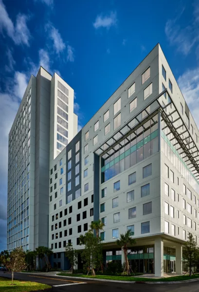 Corner view of tall modern building with glass entrance and palm trees