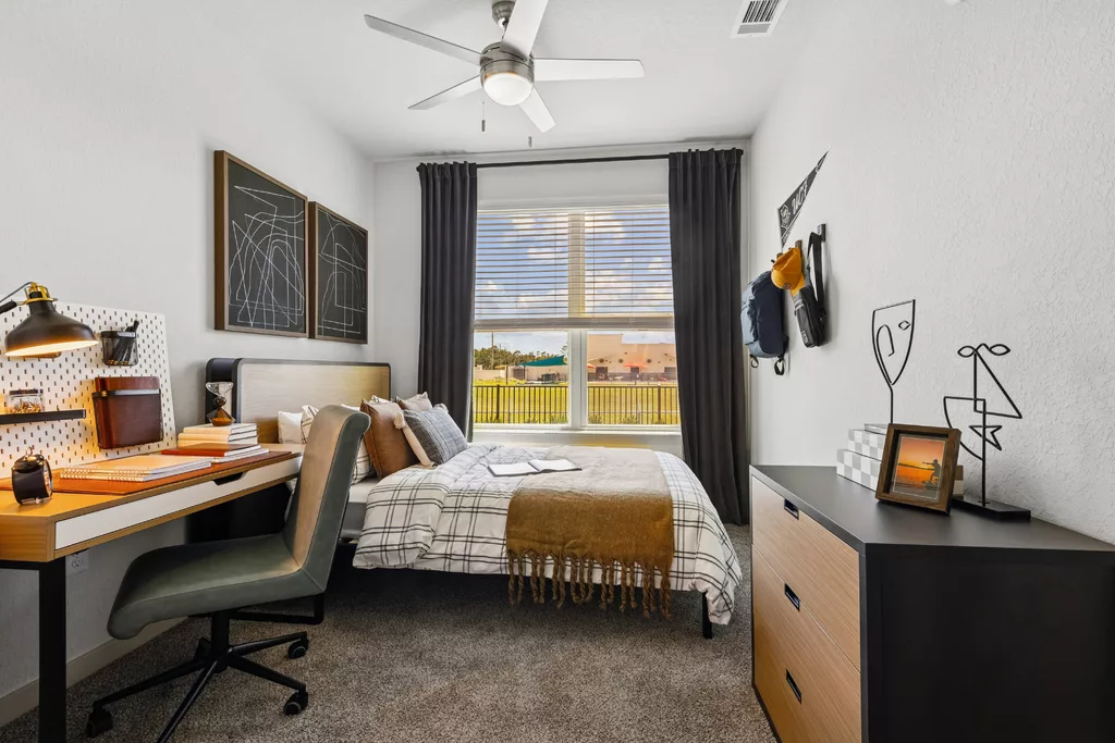 Bedroom with bed, study desk, dresser, and large window