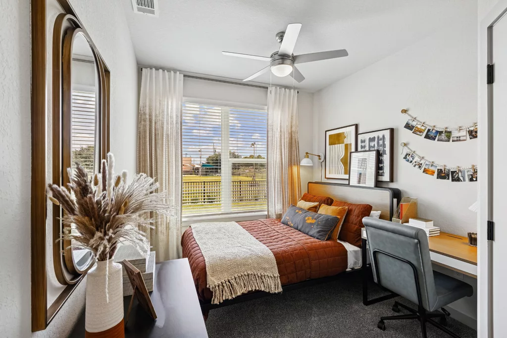 Bedroom with brown bedding, desk, art, and large window