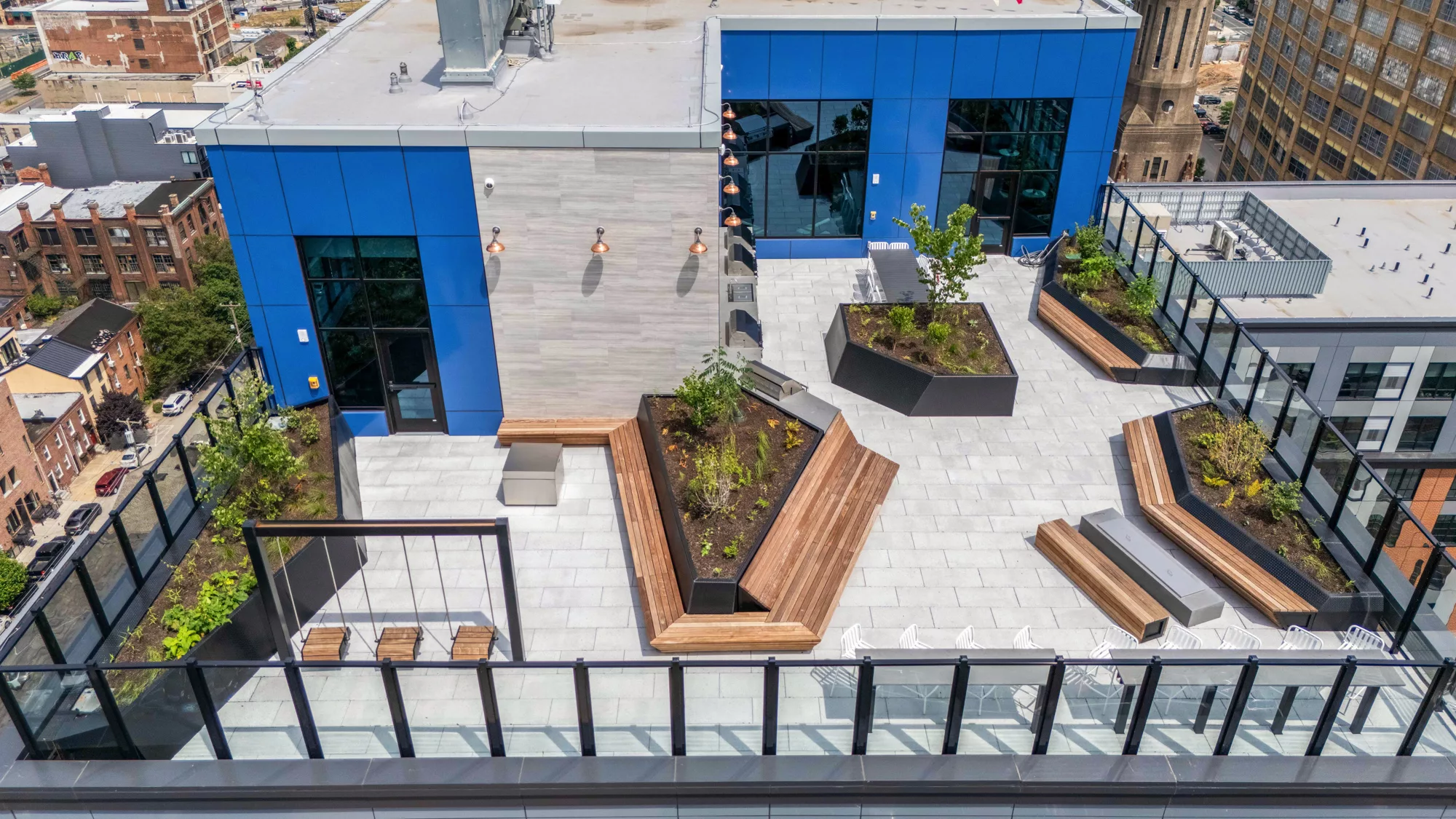 Rooftop terrace with benches, planters, swings, and glass railing