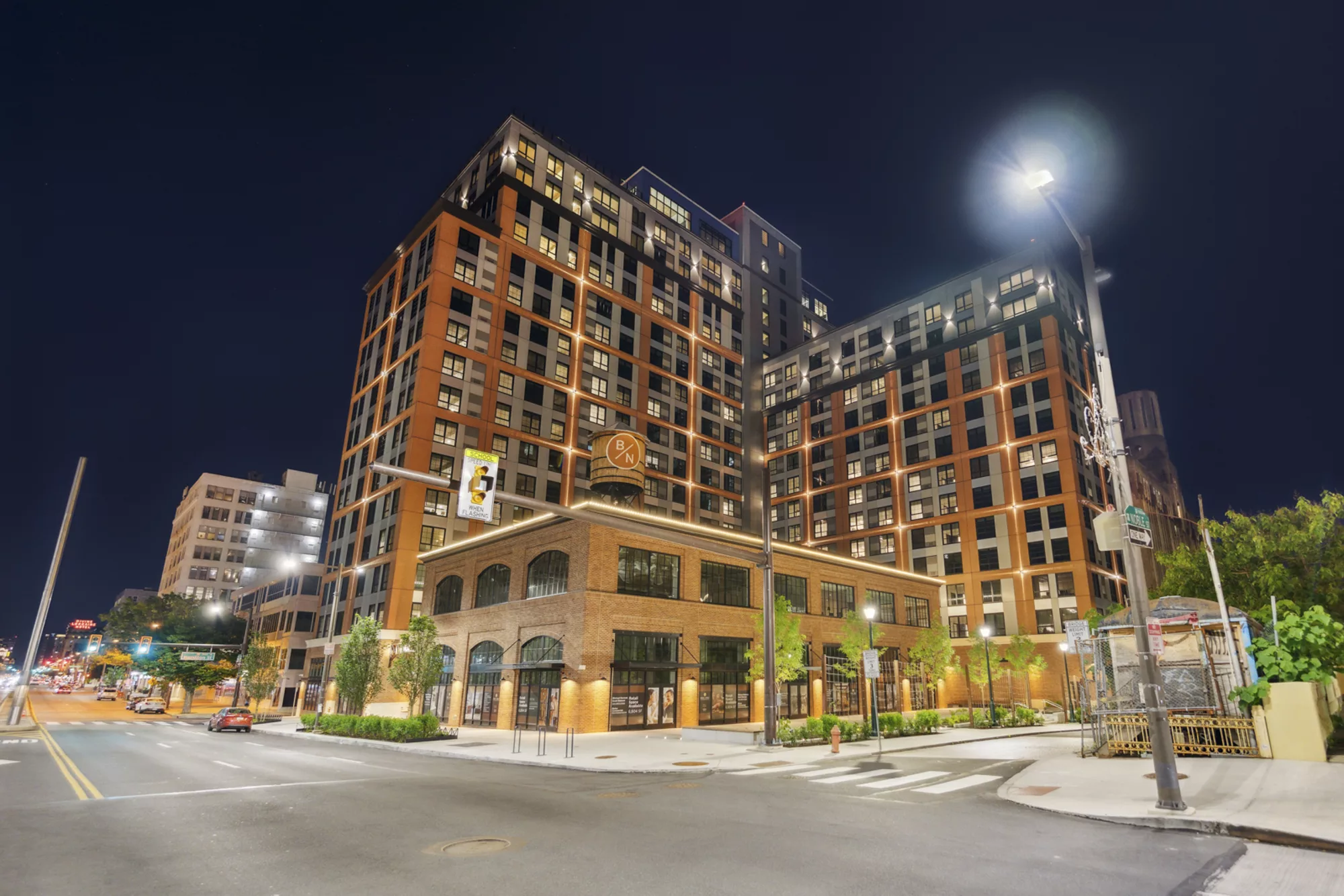 Modern multi-story apartment building illuminated at night on a city street corner.