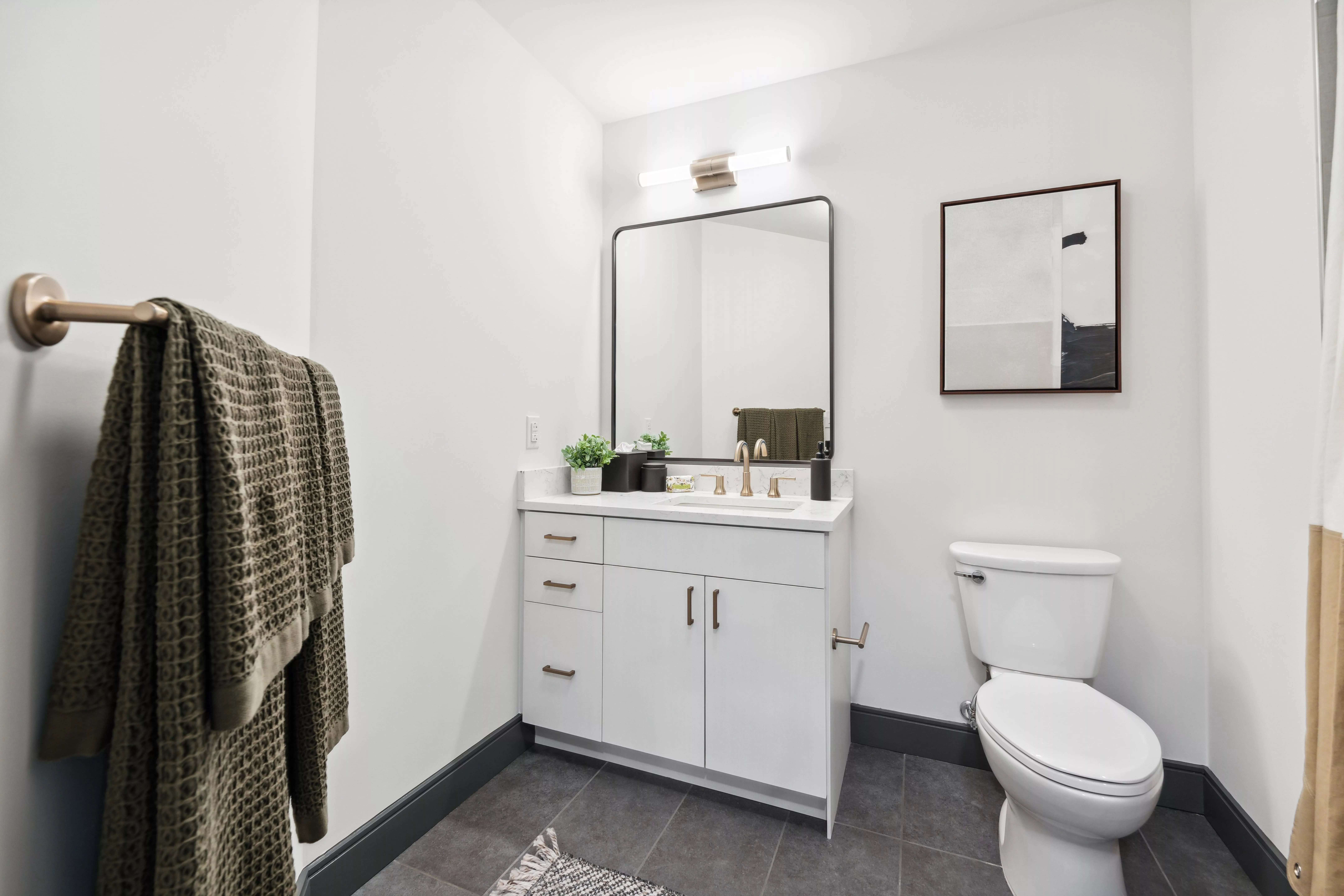 Modern bathroom with white vanity, gold fixtures, and abstract wall art.