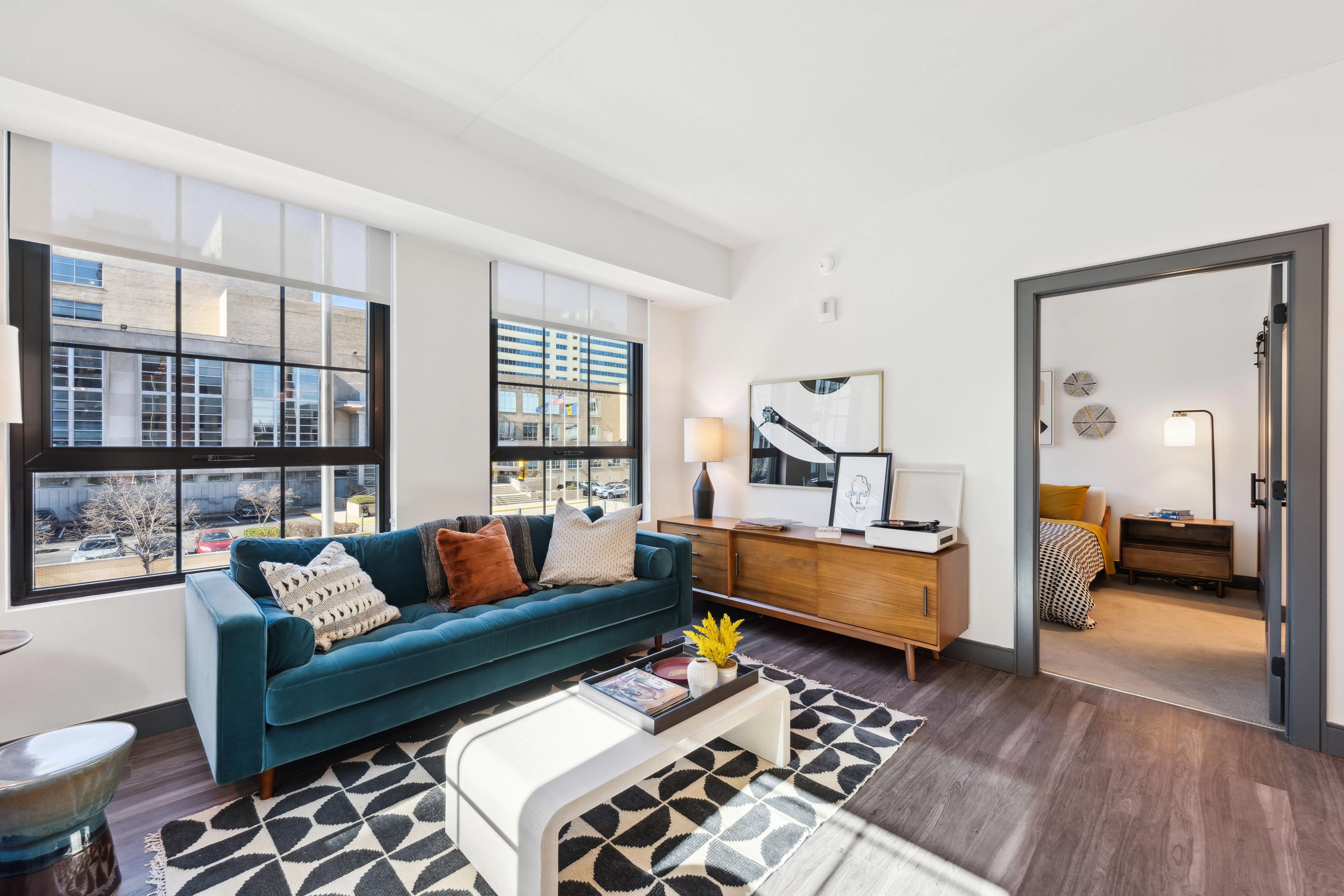 Living room with teal sofa, wood console, and large windows