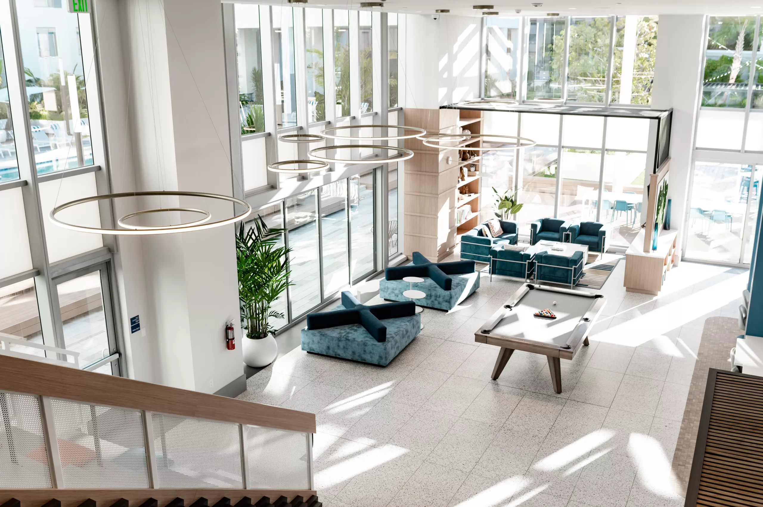 Two-story lounge with teal seating, pool table, and large windows