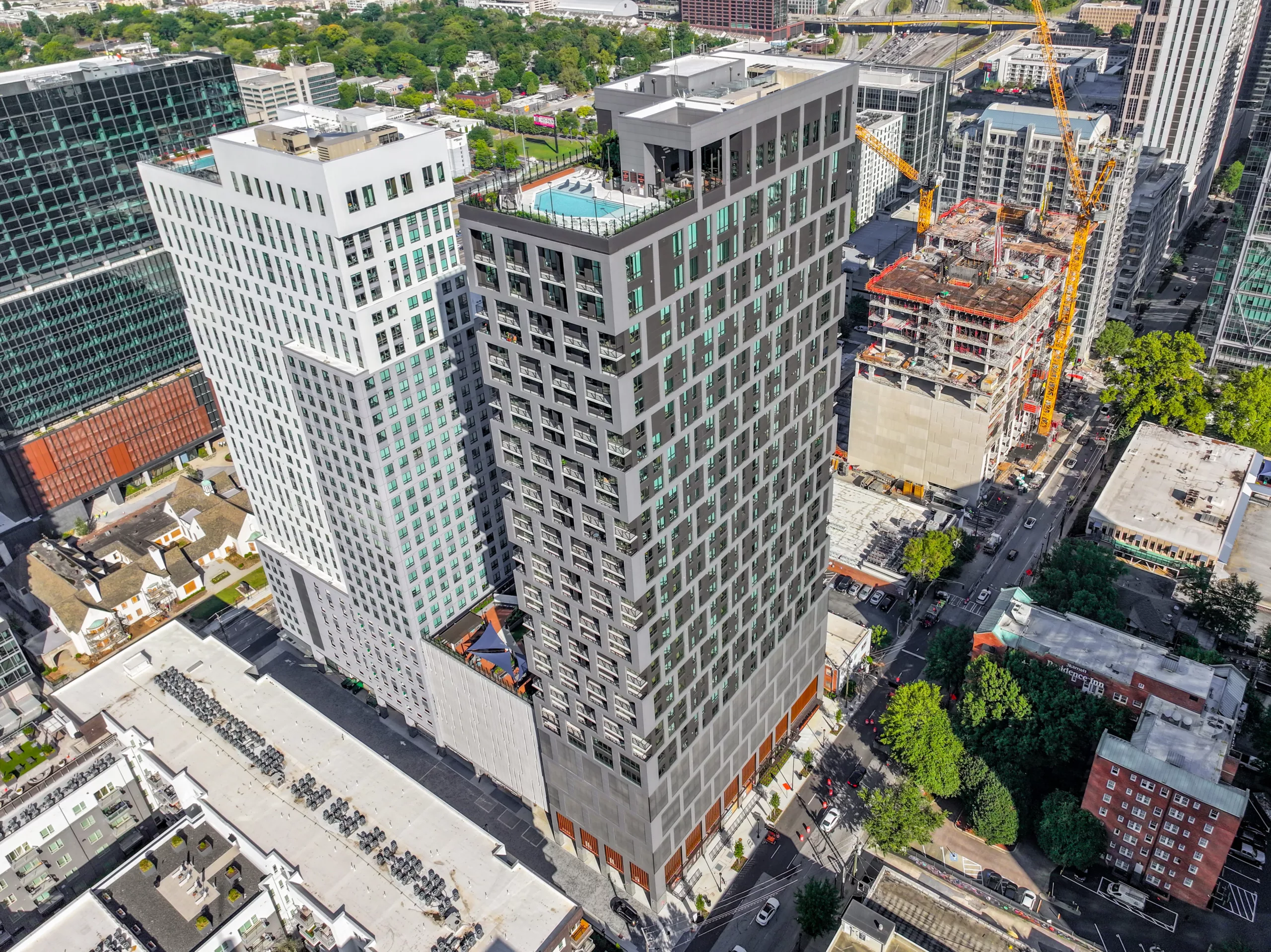 Tall modern apartment building with rooftop pool in a busy urban area.