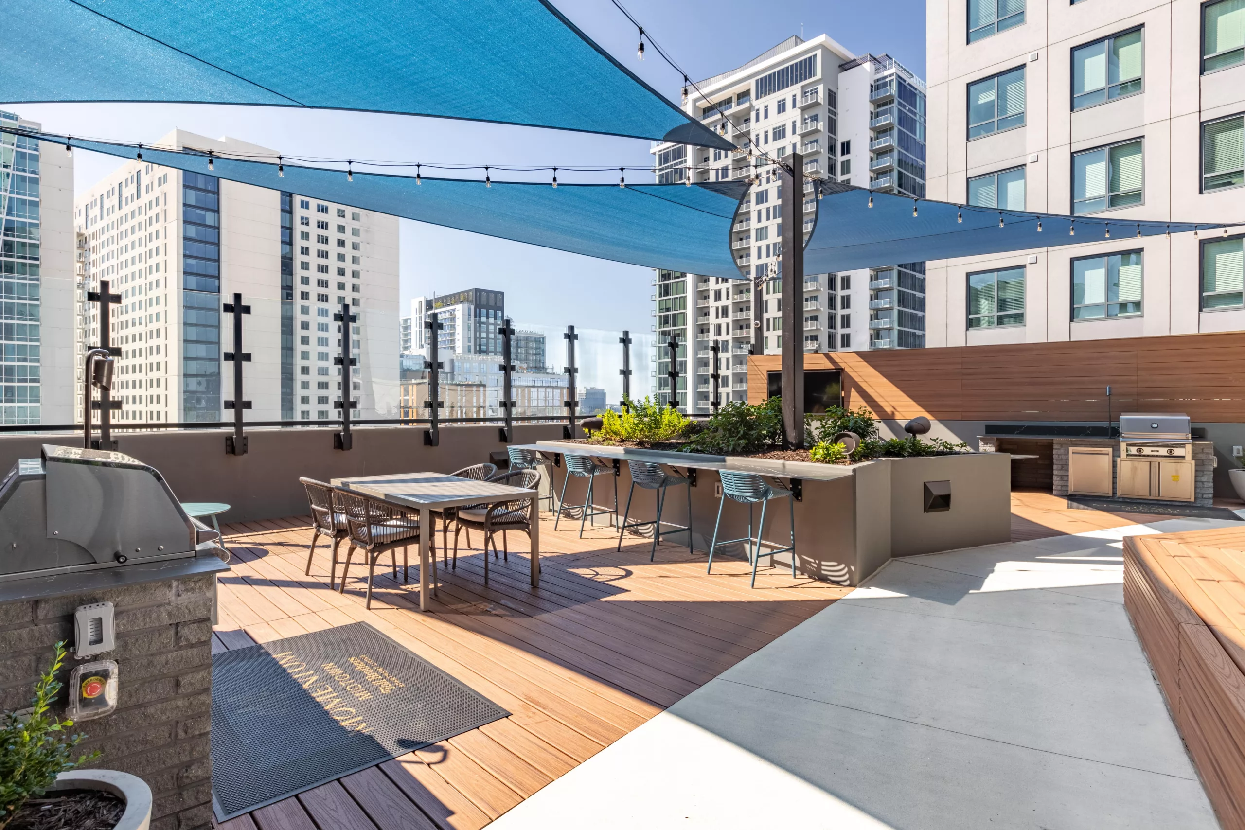 Rooftop deck with shade sails, bar seating, dining tables, and grill stations.