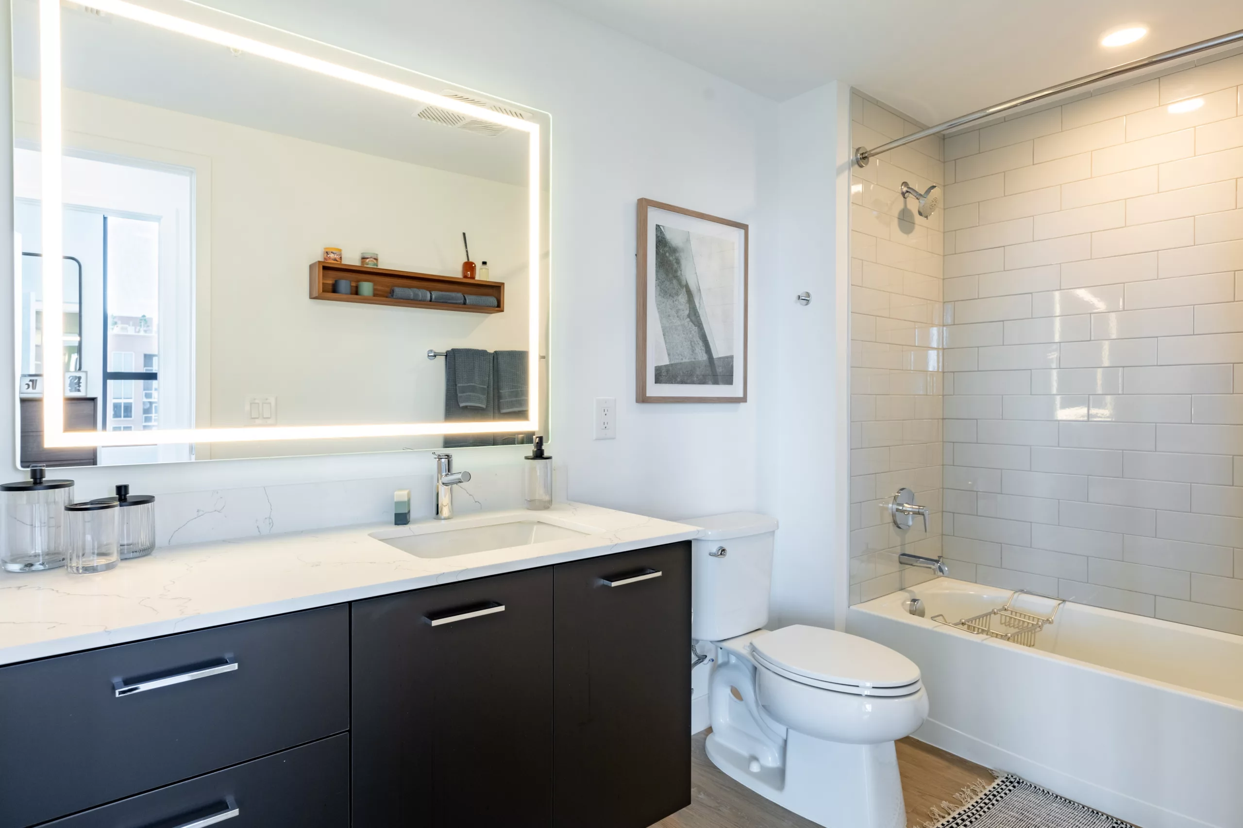 Contemporary bathroom with backlit mirror, white tile, and sleek vanity.
