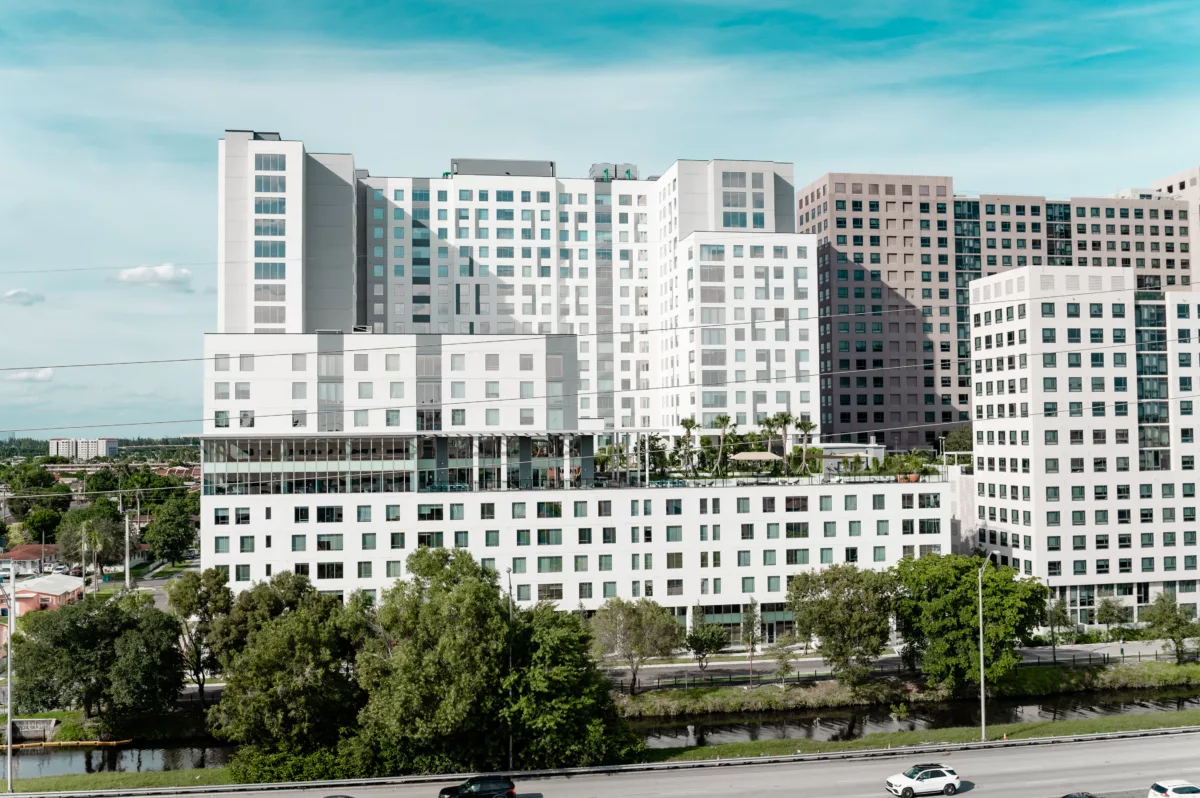 White high-rise complex with rooftop greenery and nearby highway view