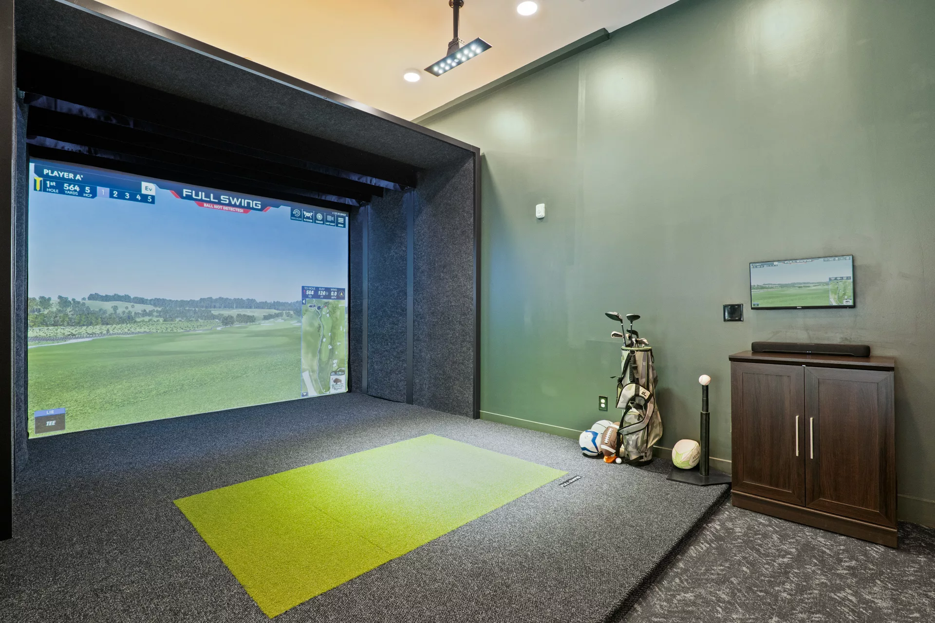 Indoor golf simulator room with screen, turf, and golf equipment.