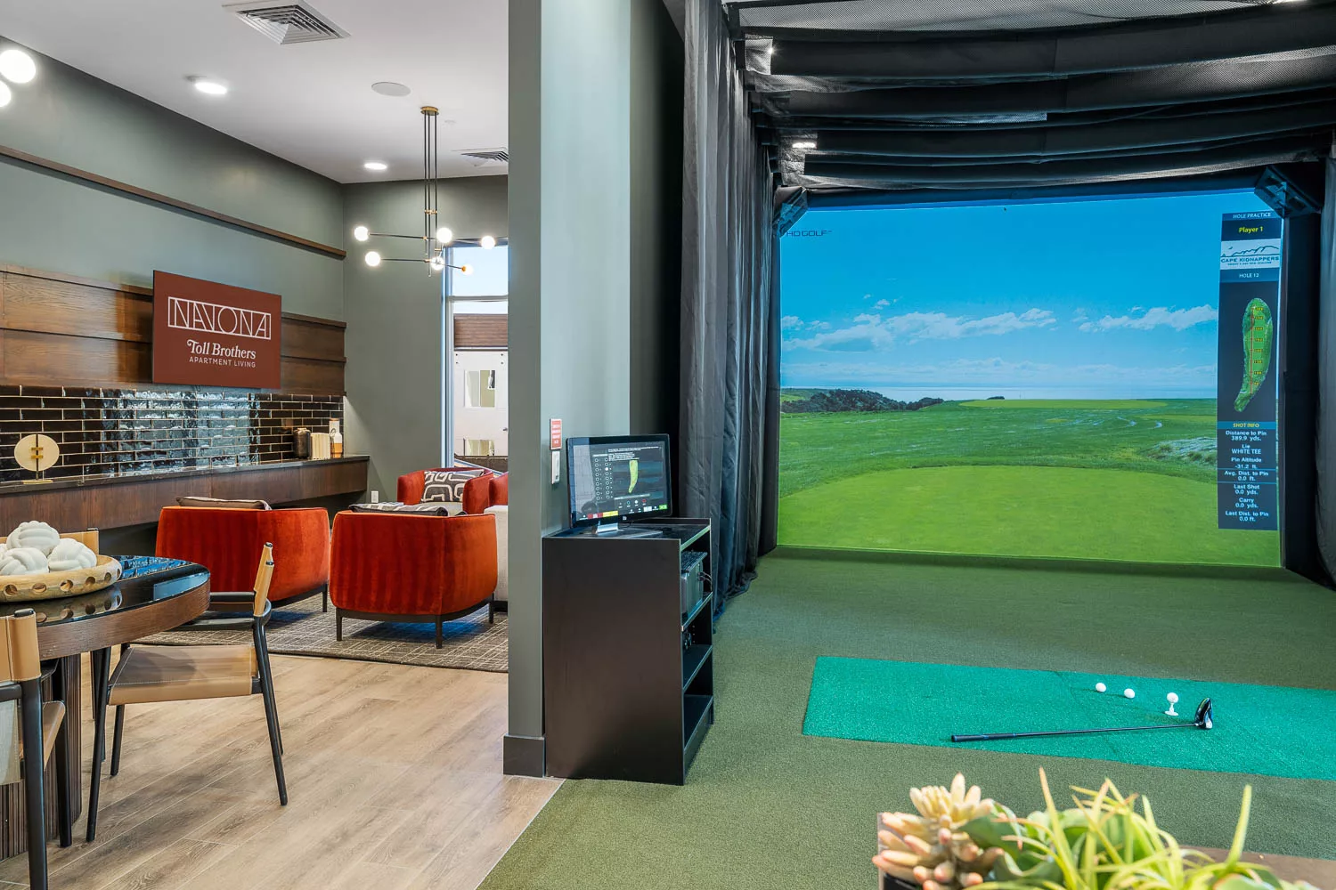 Indoor golf simulator next to lounge area with red chairs.