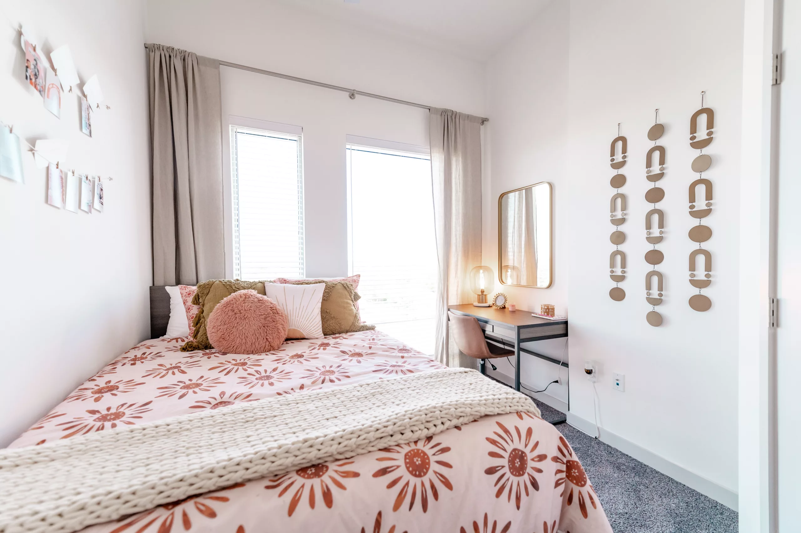 Bedroom with floral bedding, wall decor, desk, and large windows with curtains