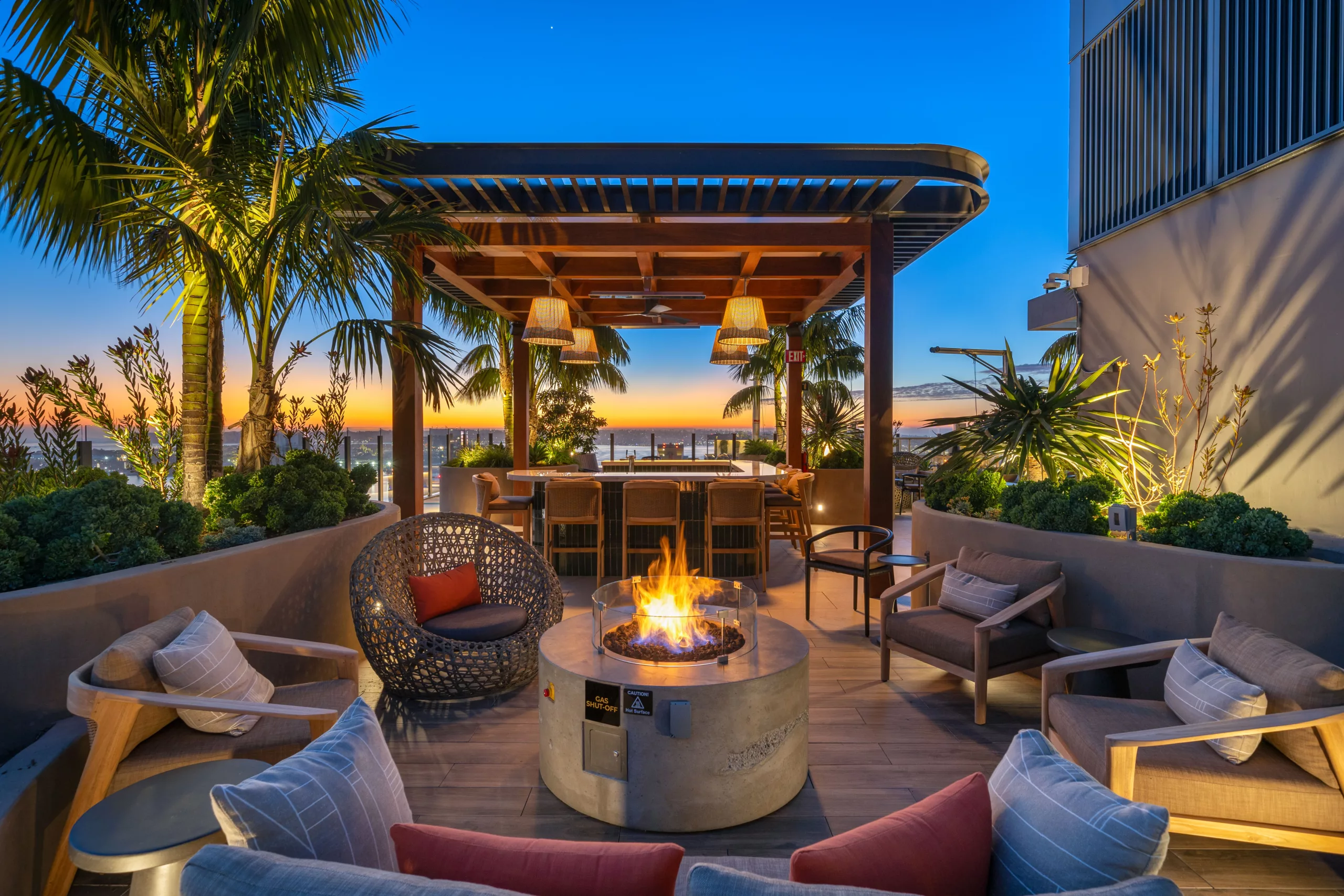 Outdoor lounge with firepit, tropical plants, and sunset view
