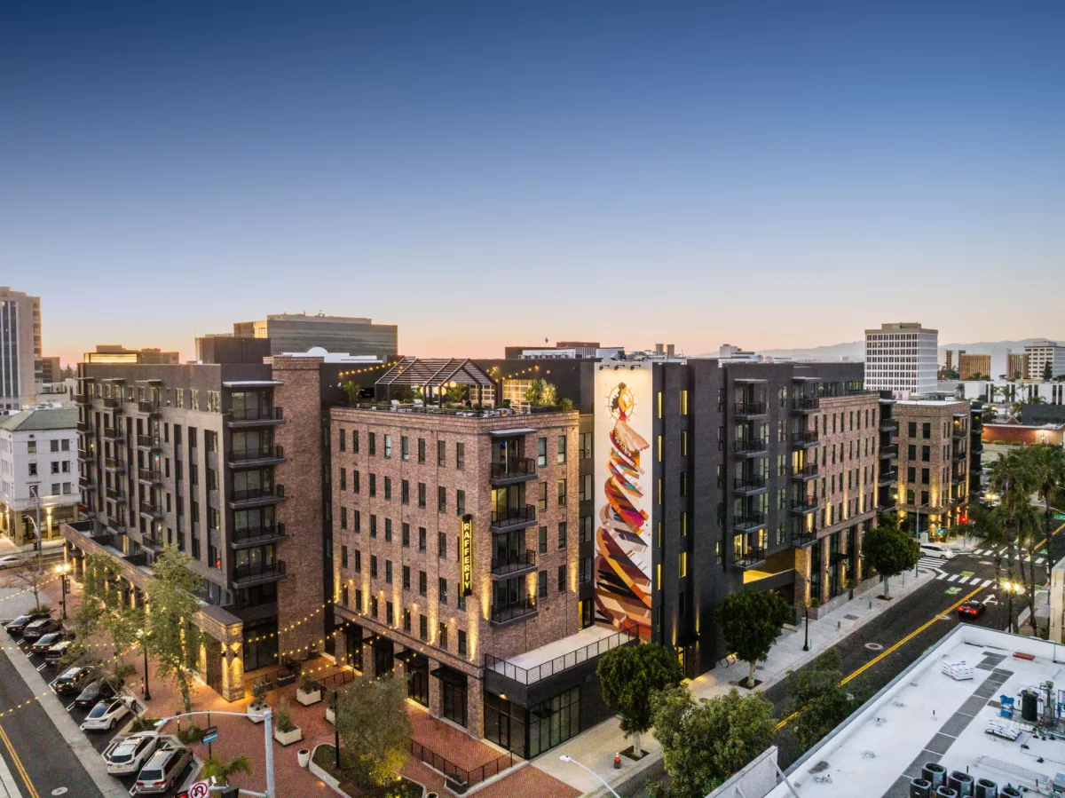 Brick apartment complex with rooftop amenities and large mural at dusk.