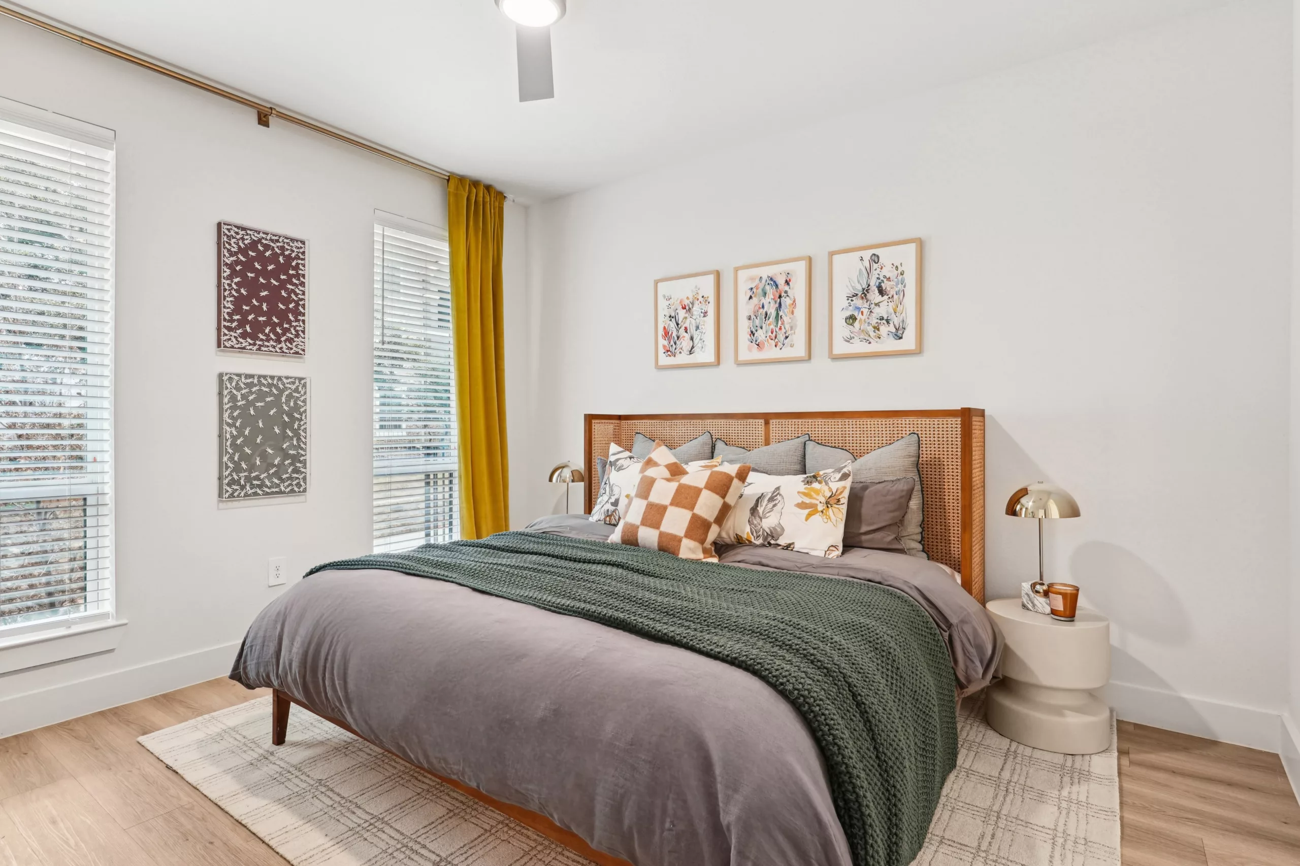 Bedroom with checkered pillow, floral art, and gold curtain.