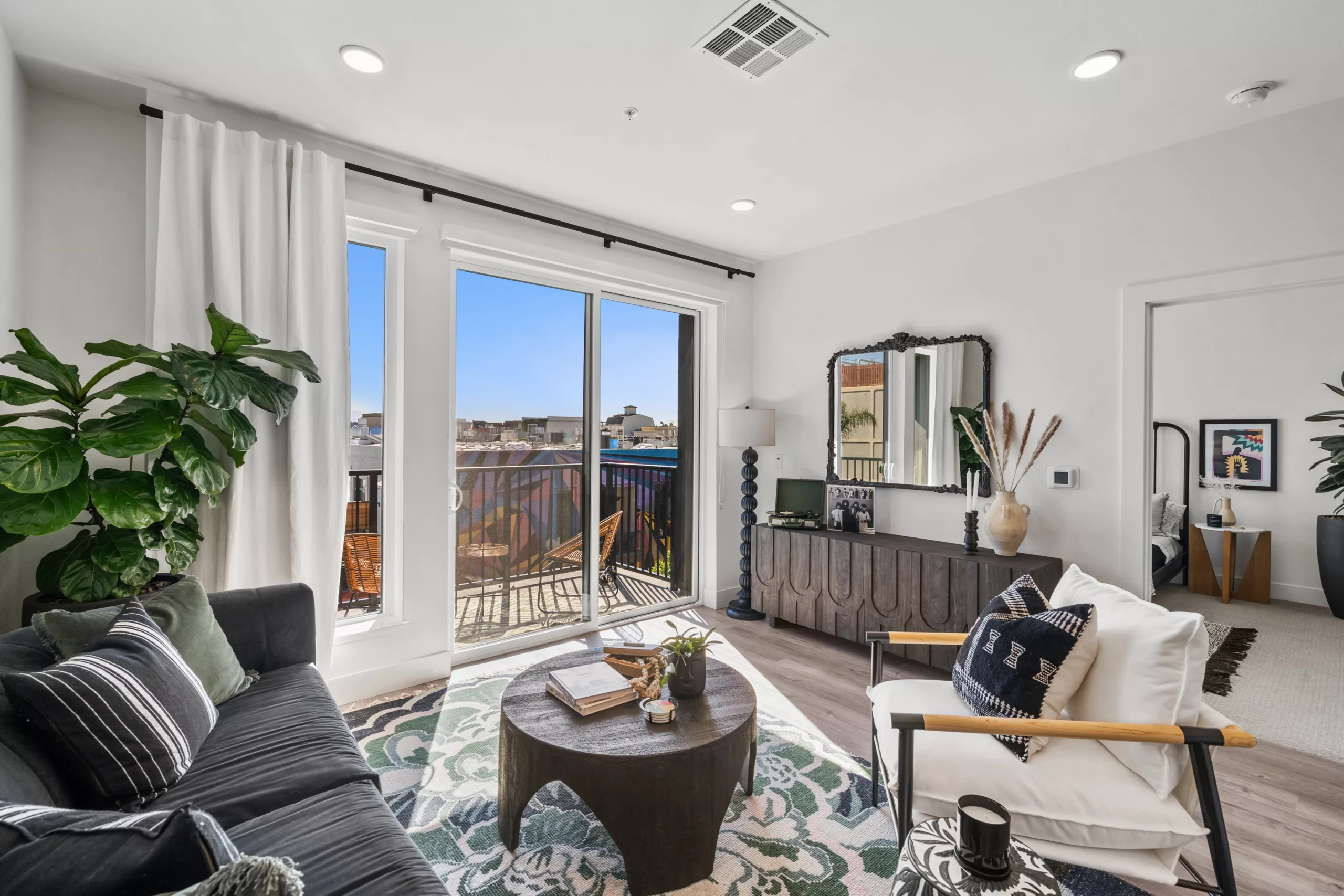 Living room with black sofa, round table, balcony access, and eclectic decor.