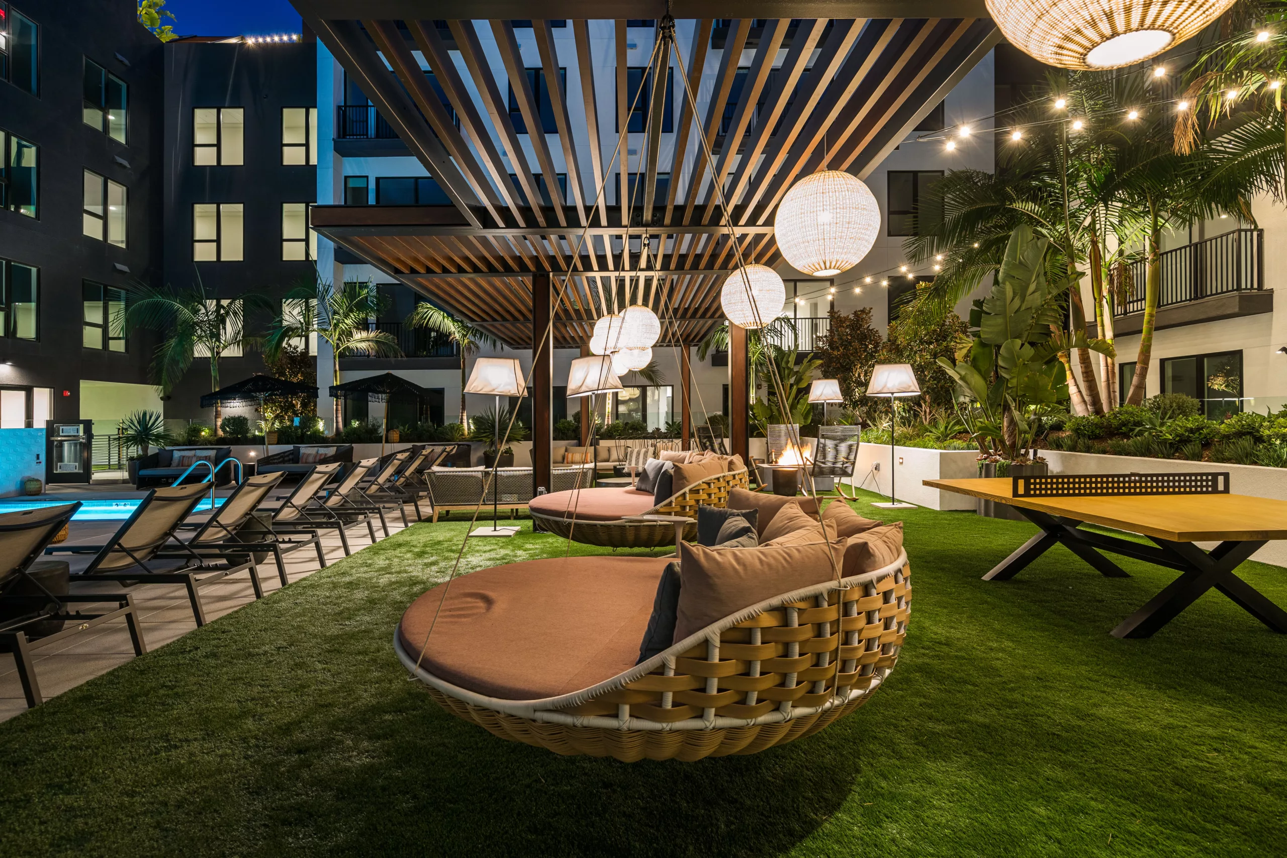 Outdoor lounge with swings, string lights, and a ping pong table.