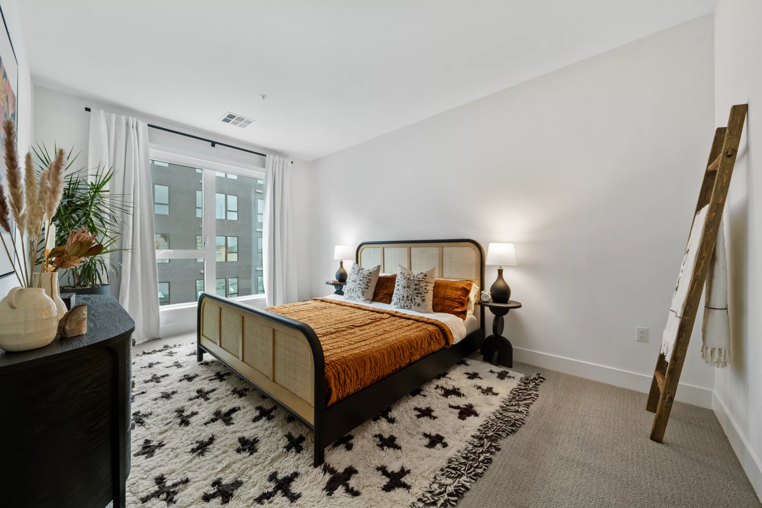 Stylish bedroom with modern decor, patterned rug, and natural light from large windows.