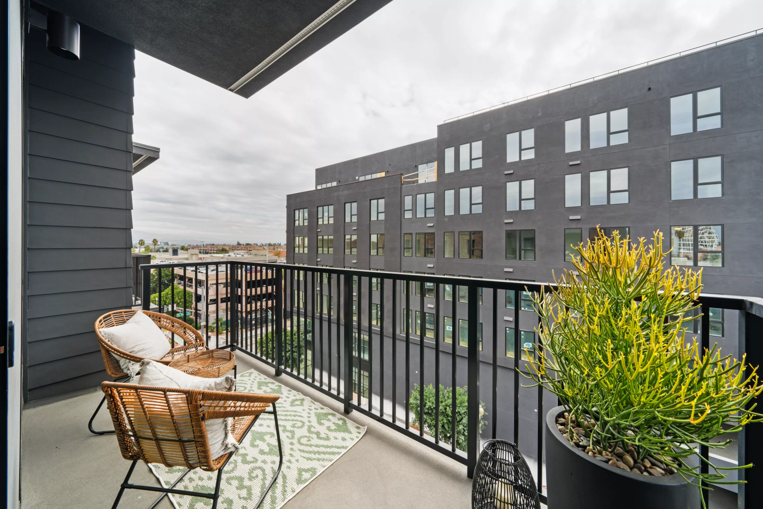 Modern apartment balcony with outdoor seating and potted plants overlooking other buildings.
