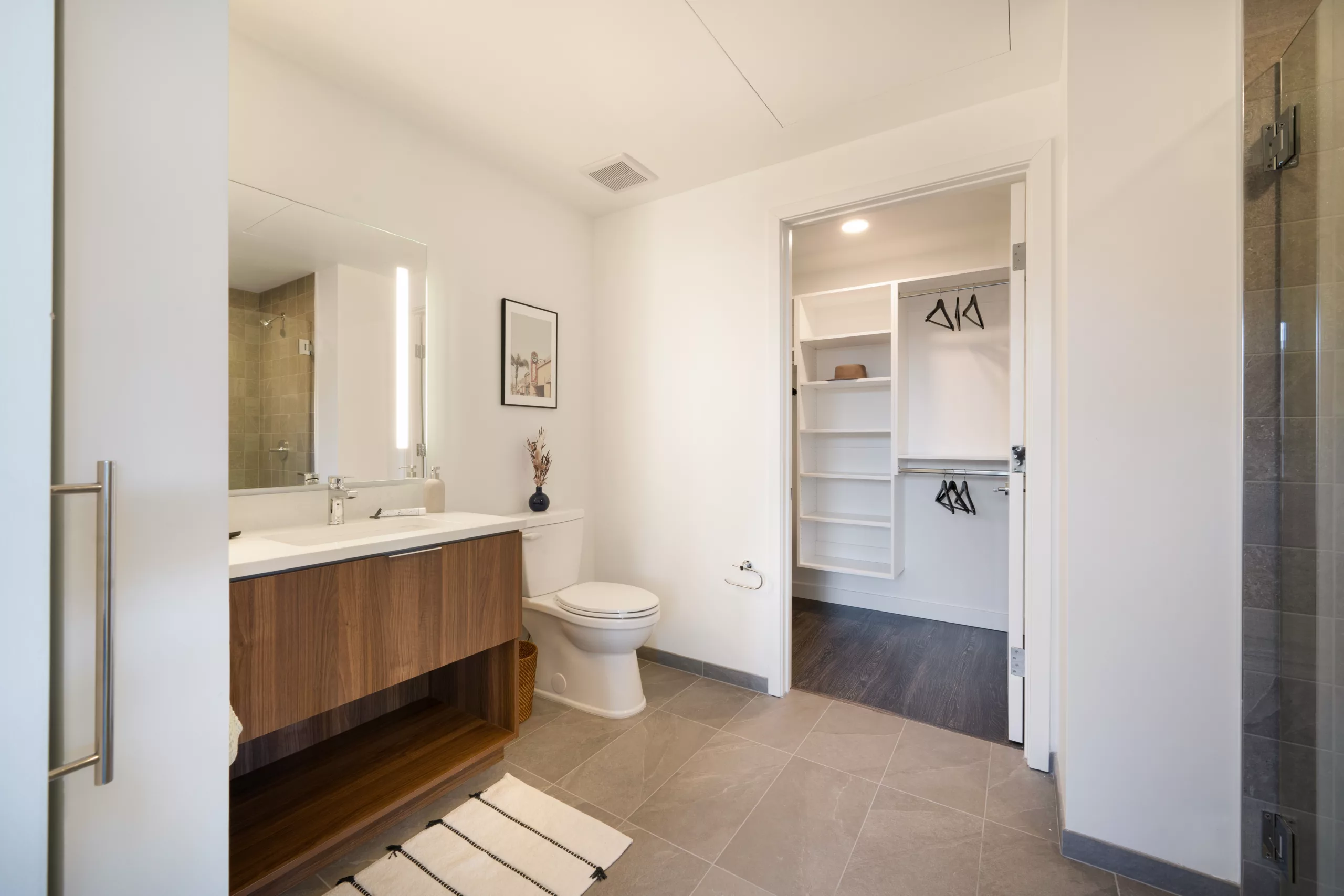 Modern bathroom with wood vanity, toilet, and walk-in closet
