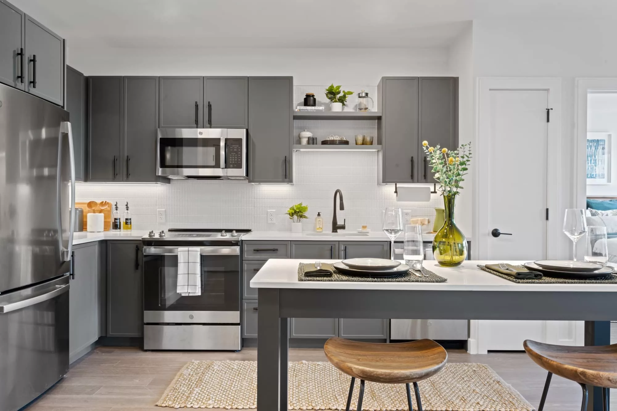 Modern kitchen with dark gray cabinets, stainless steel appliances, and a dining island set with plates and a vase of flowers.