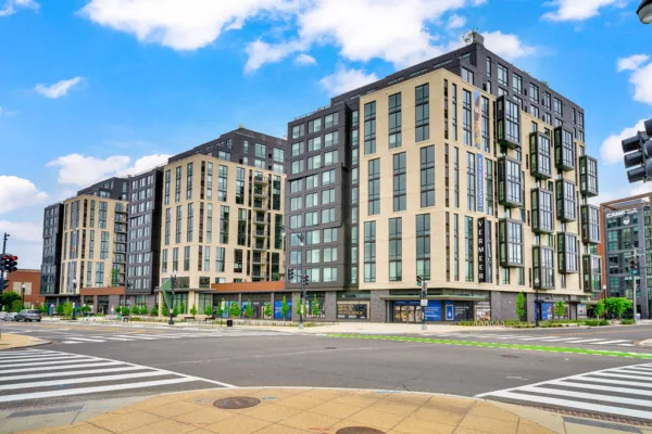 Modern multi-story apartment complex with ground-level retail at a city street intersection.