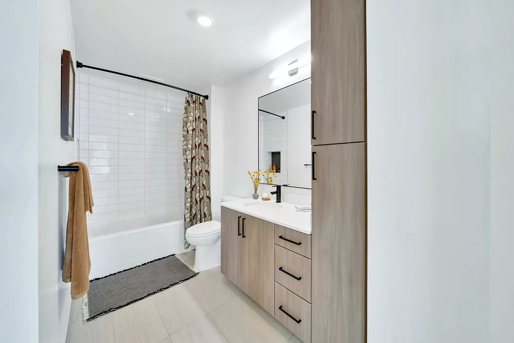 Modern bathroom with wood cabinetry, tub with curtain, and large wall mirror