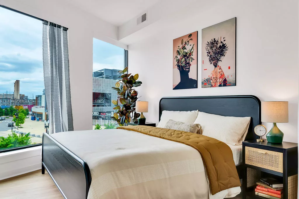 Bedroom with black bedframe, city view window, and abstract art above bed