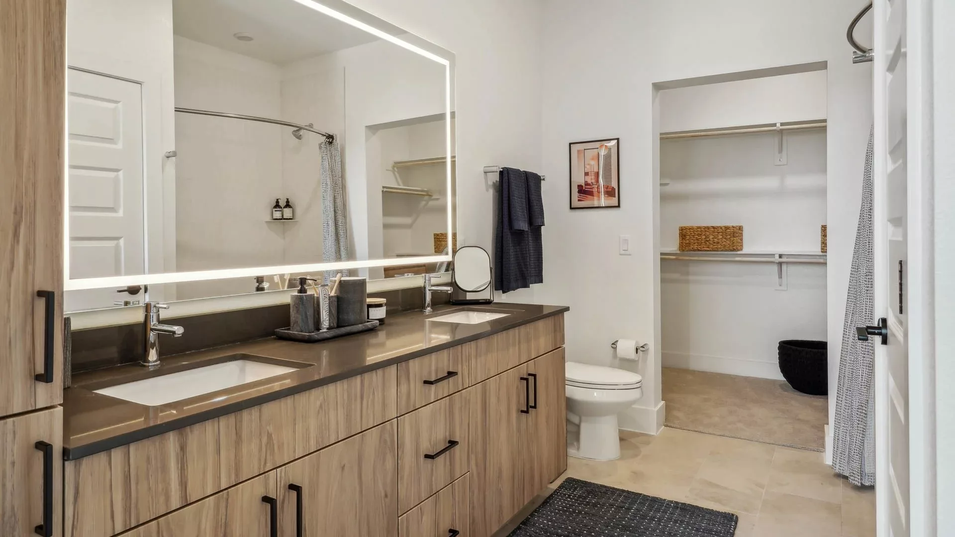 Bathroom with dual sinks, wood cabinetry, and walk-in closet