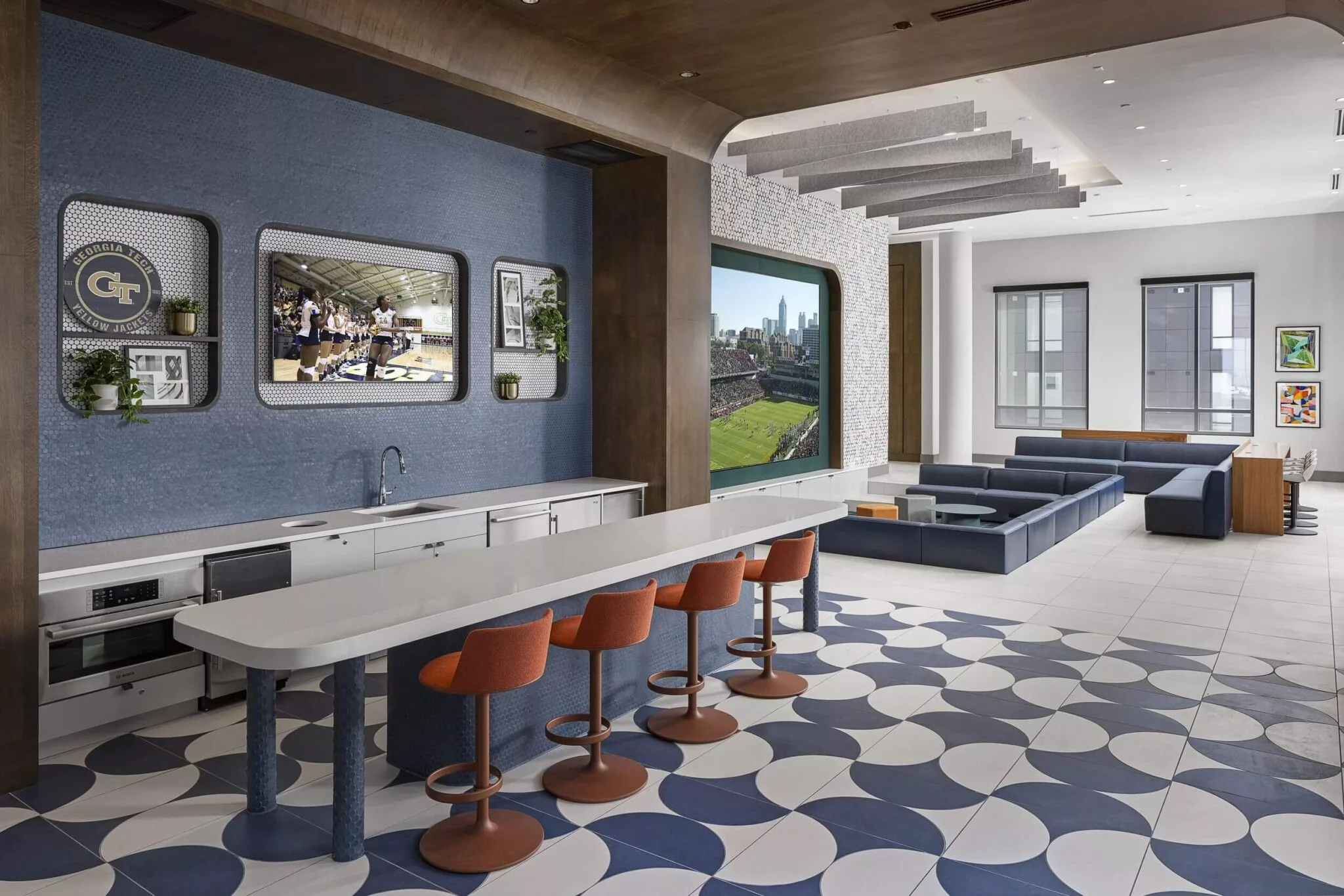 Spacious lounge area with large TV screens, bar seating, modern decor, and blue-and-white geometric flooring.