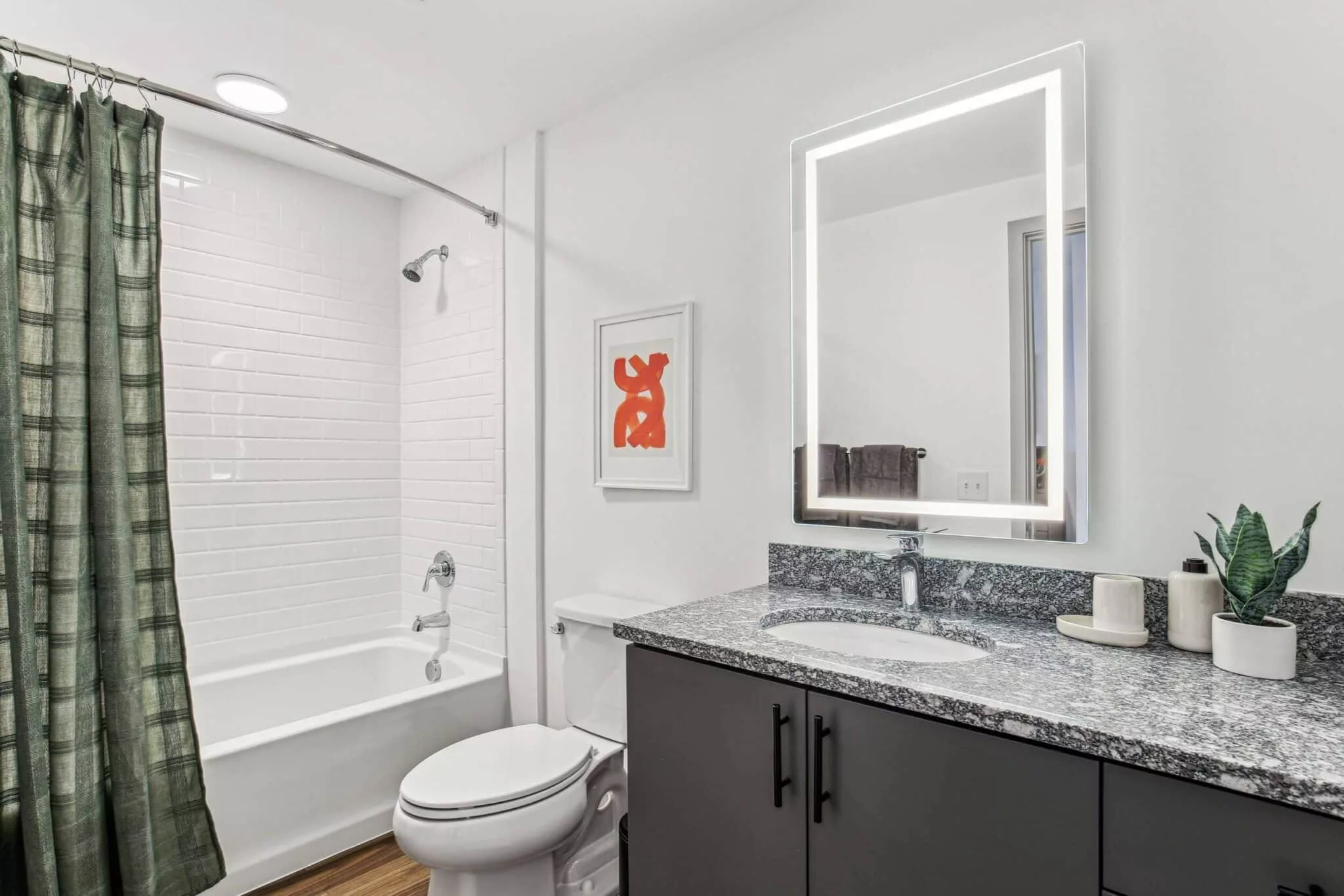 Bright bathroom with granite countertop, lighted mirror, white tile shower with curtain, and modern fixtures.