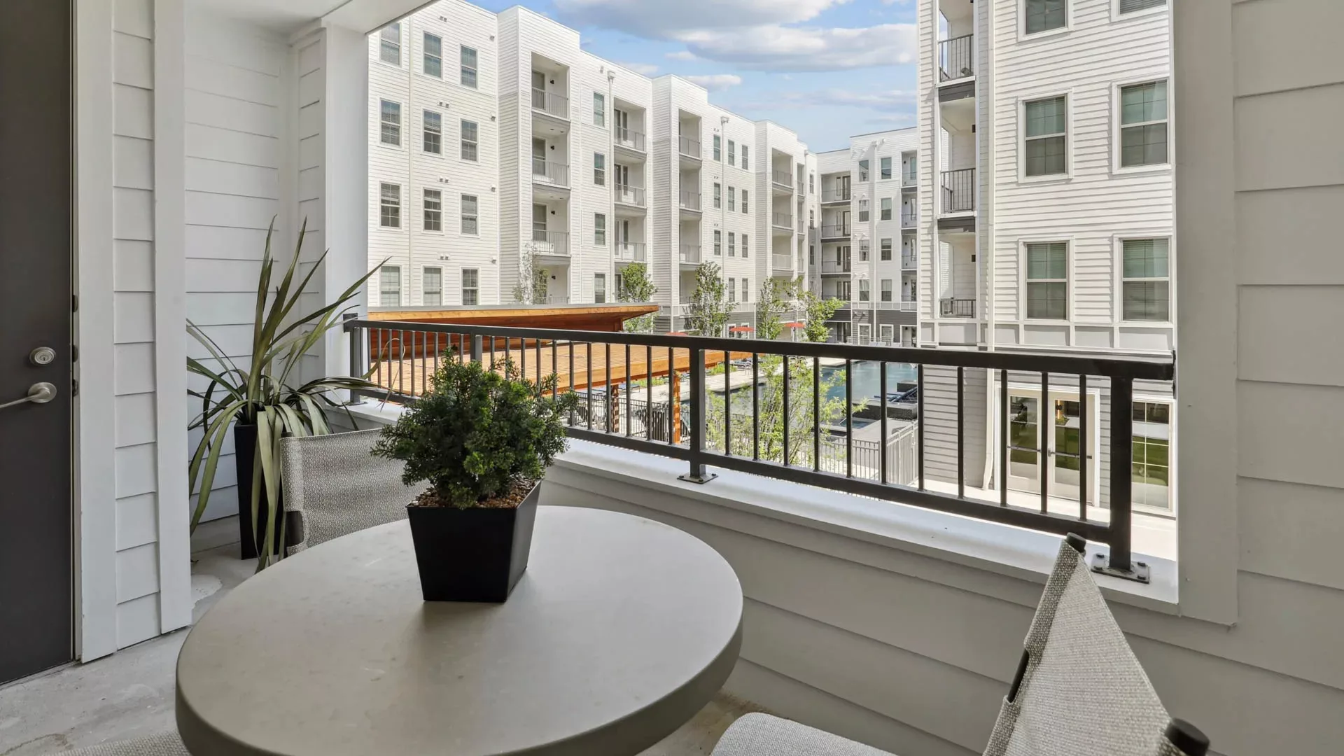 Balcony with small table, chairs, potted plants, and view of courtyard