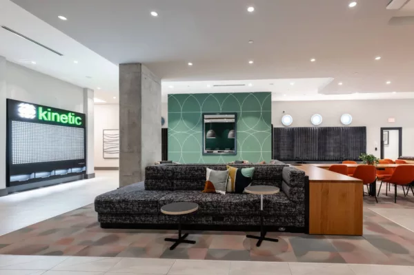 Stylish lounge with curved seating, green feature wall, and communal tables with bright orange chairs.