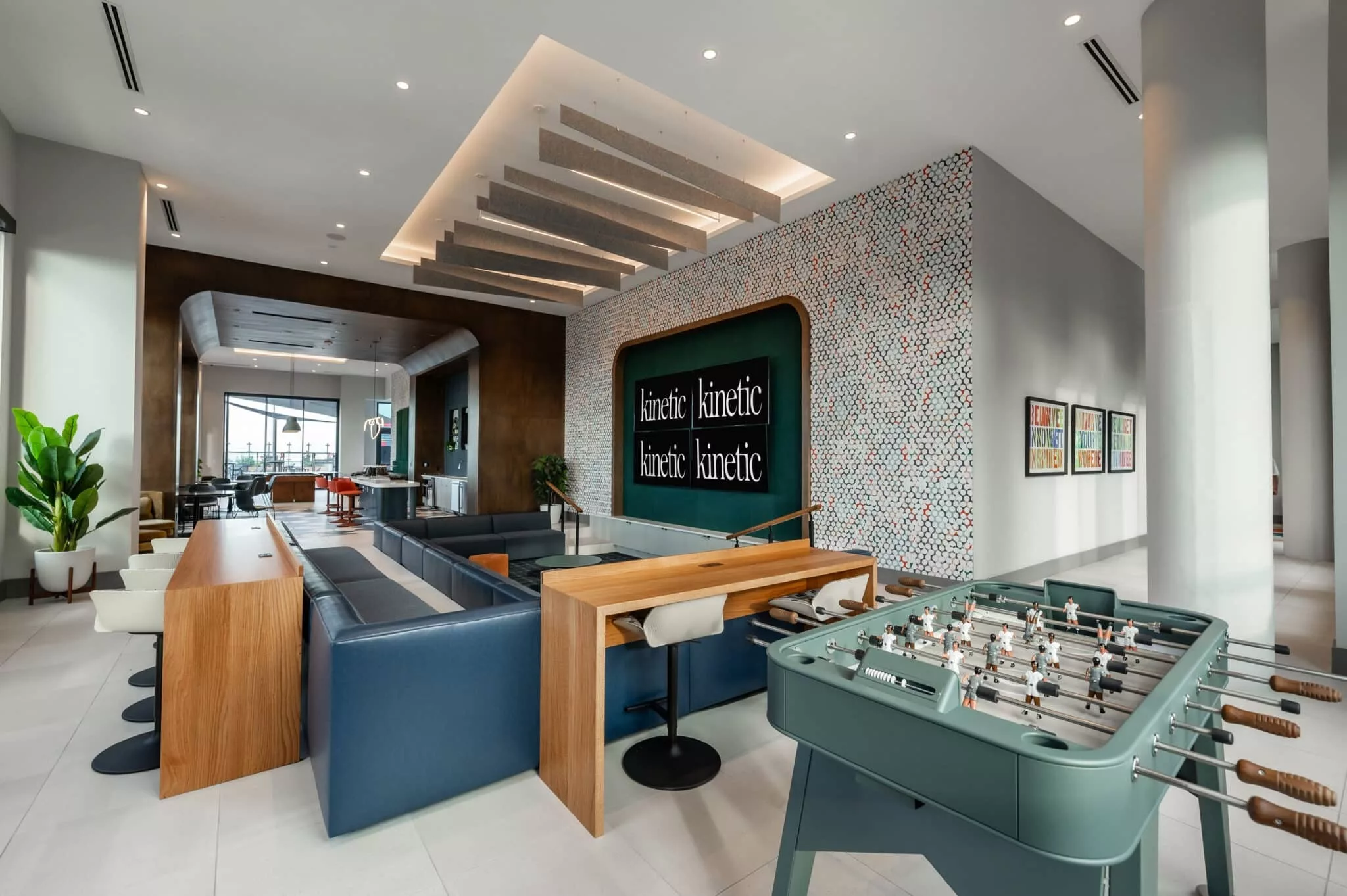 Contemporary co-working and entertainment space featuring multiple “kinetic” branded screens, foosball table, and lounge seating.