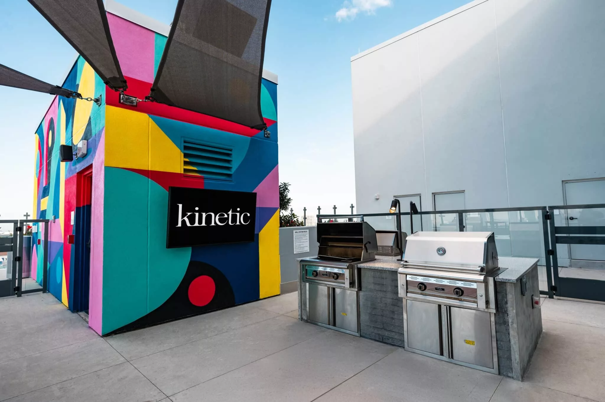Rooftop grilling station with two stainless steel barbecue grills next to a vibrant mural and kinetic signage.