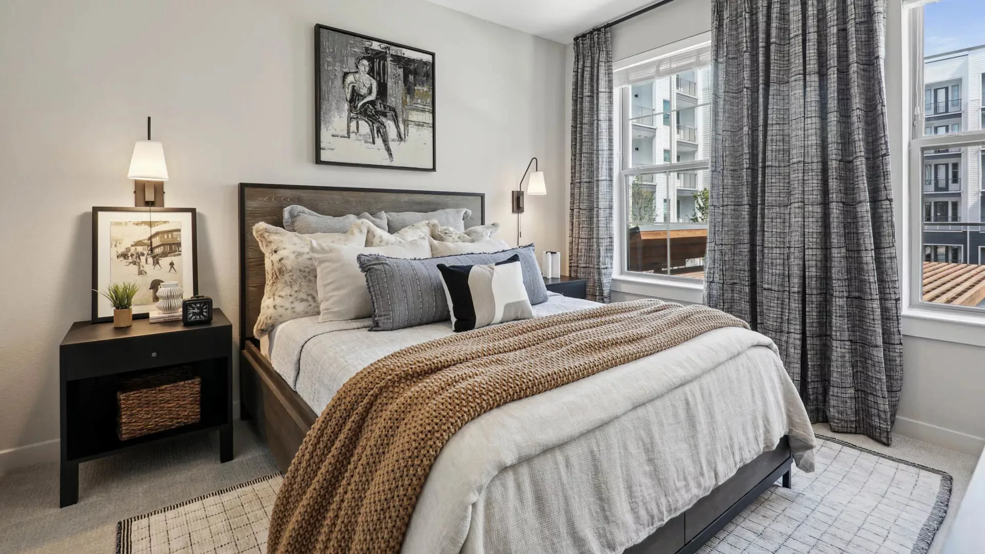 Bedroom with large bed, modern decor, and window view of apartment complex