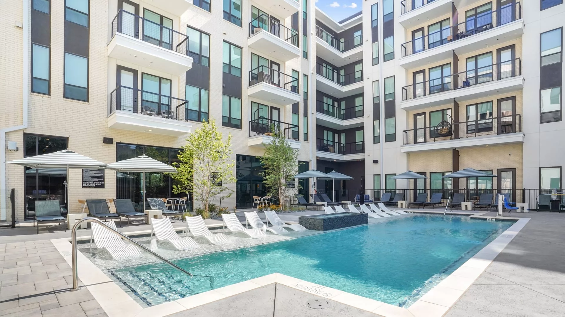 Outdoor pool with lounge chairs, umbrellas, and modern apartment balconies