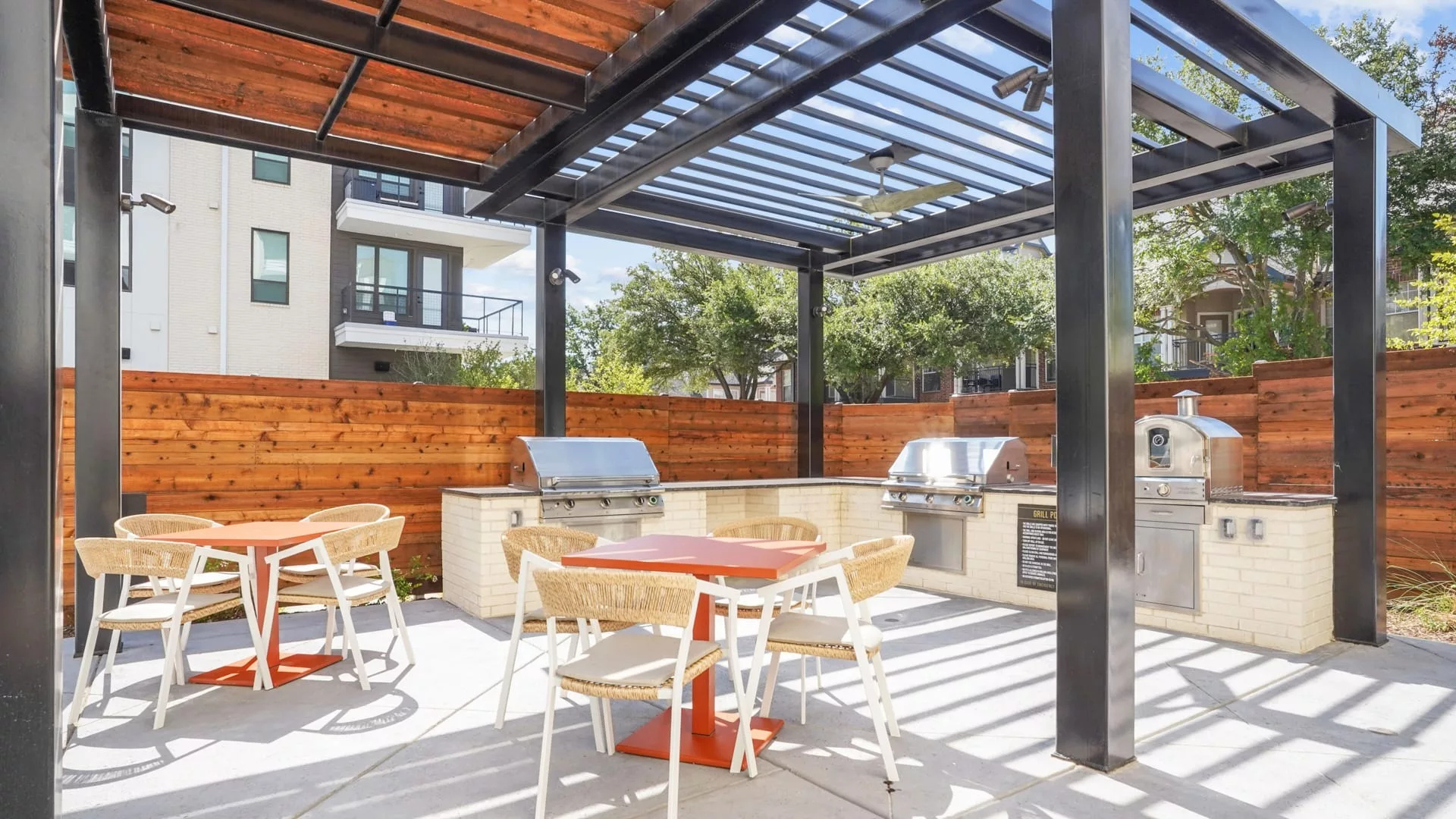 Covered outdoor kitchen with grills, tables, and wood-paneled fencing