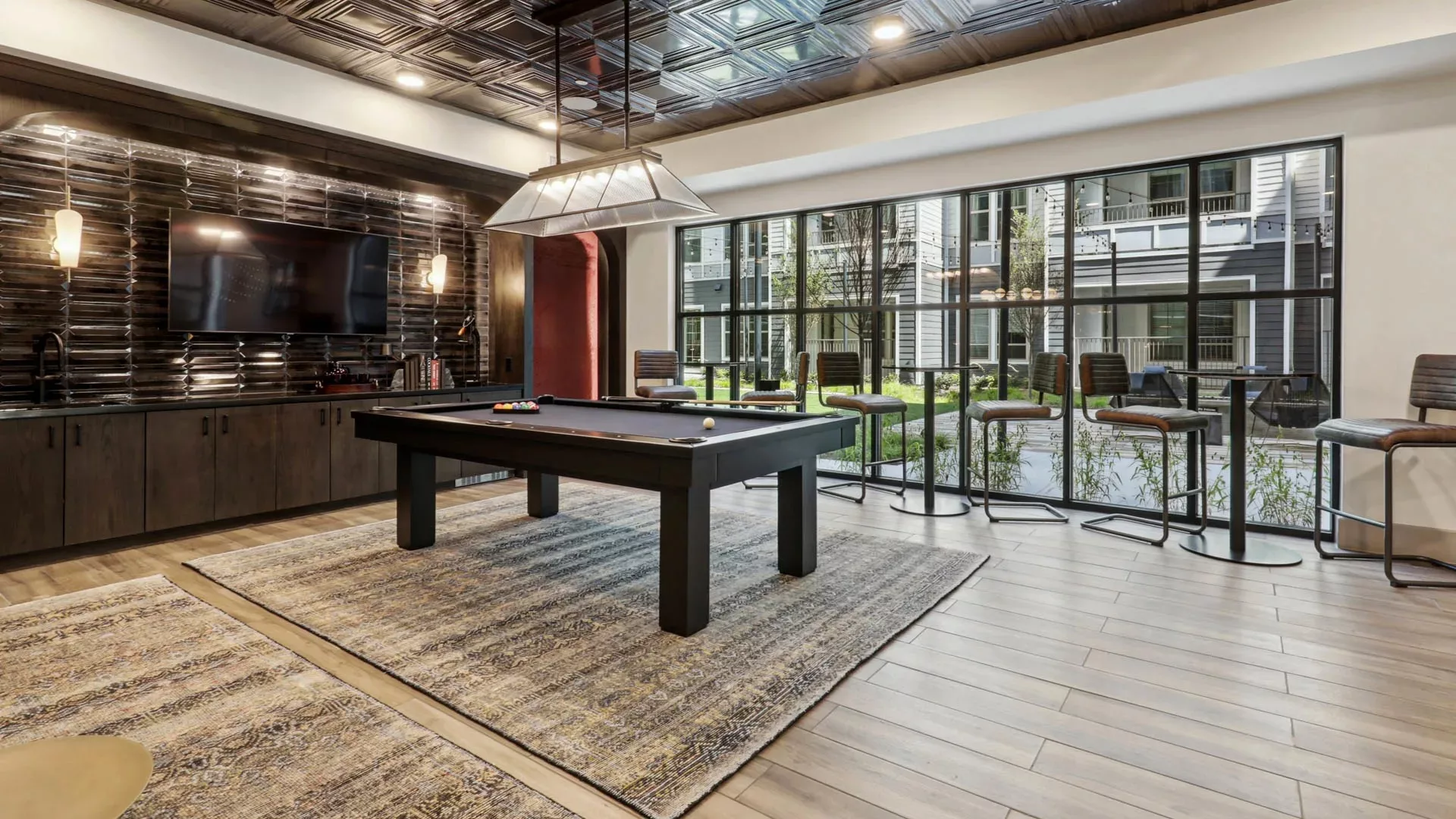 Pool table room with bar seating and view of courtyard through large windows
