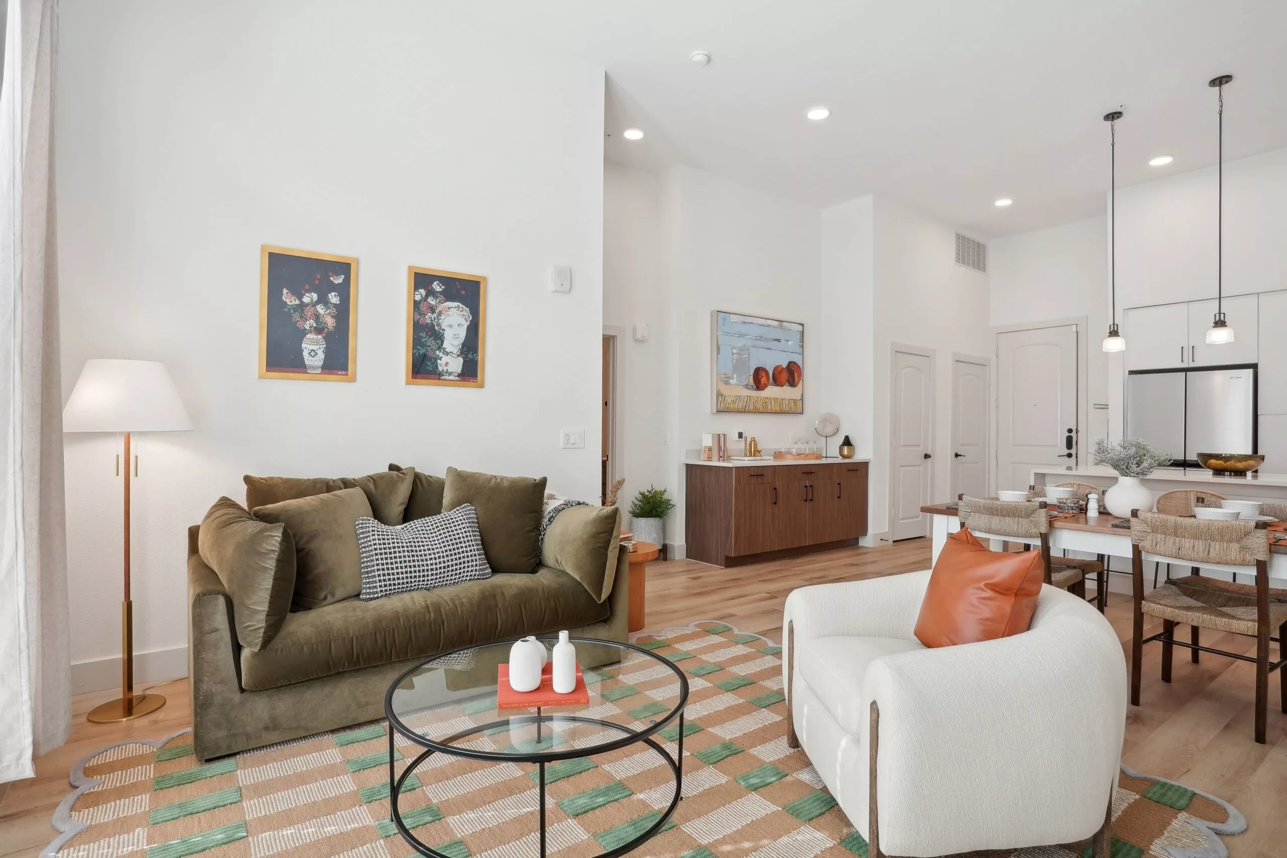 Living room with olive green couch, white armchair, and round glass coffee table