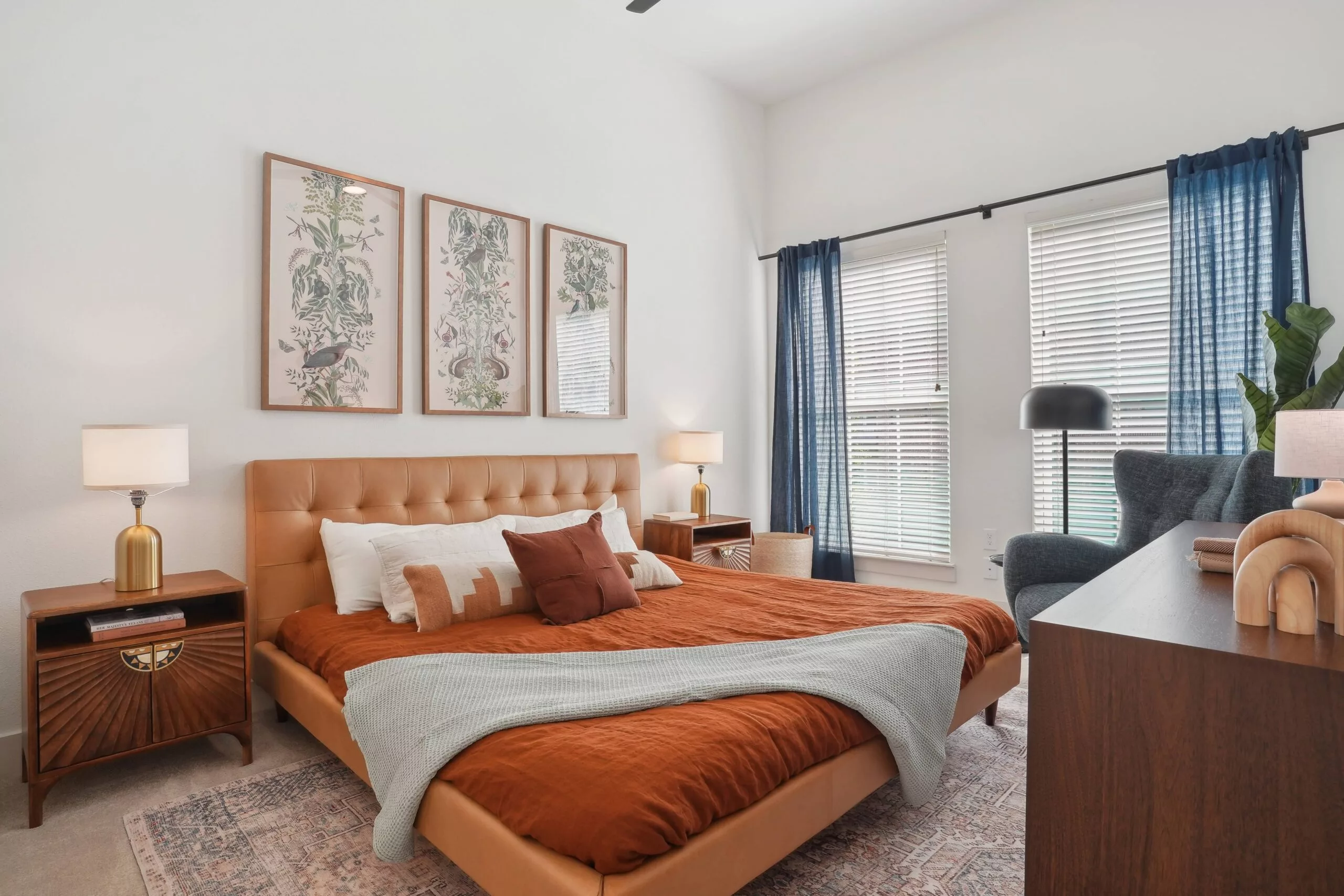 Bedroom with tan tufted bed, rust-colored bedding, and botanical wall art