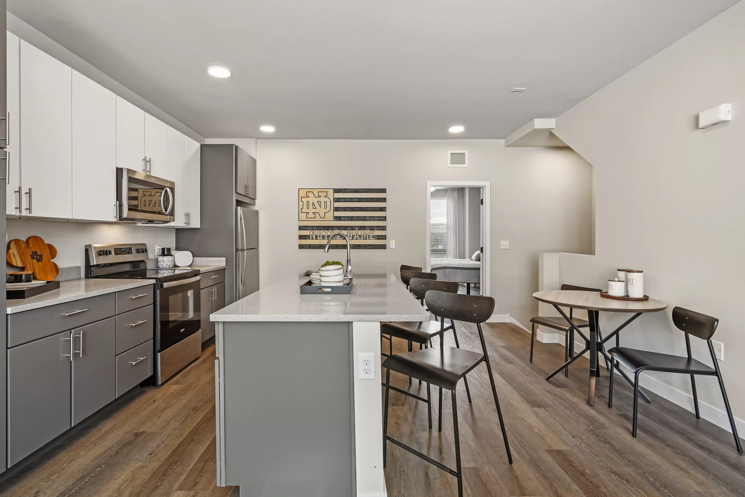 Modern kitchen with gray and white cabinets, stainless steel appliances, center island with bar stools, and a small round dining table.