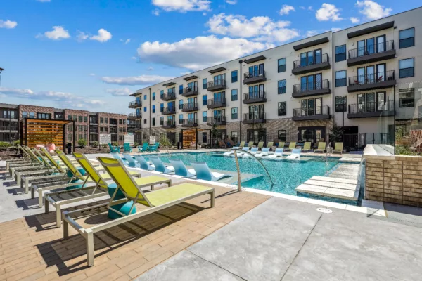 Outdoor pool area with lounge chairs and four-story apartment backdrop