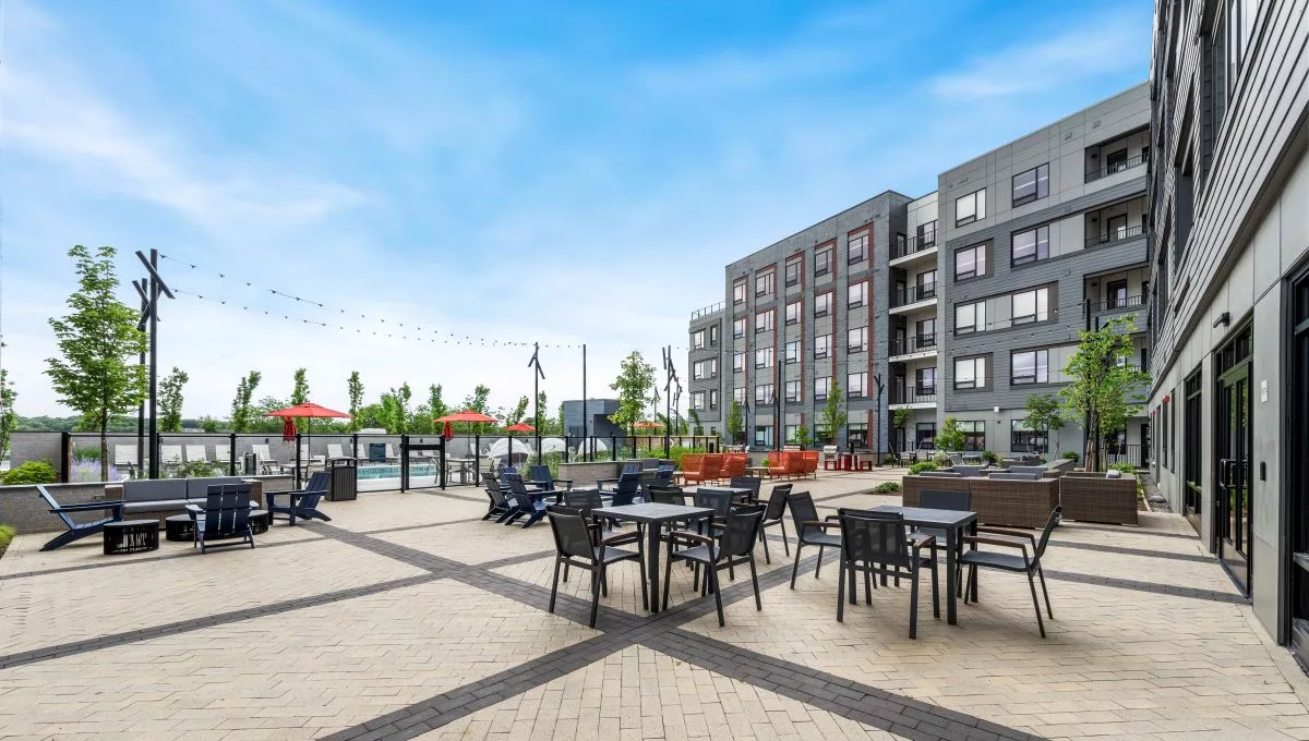The courtyard of an apartment building with tables and chairs, firepits, and a pool in the background.