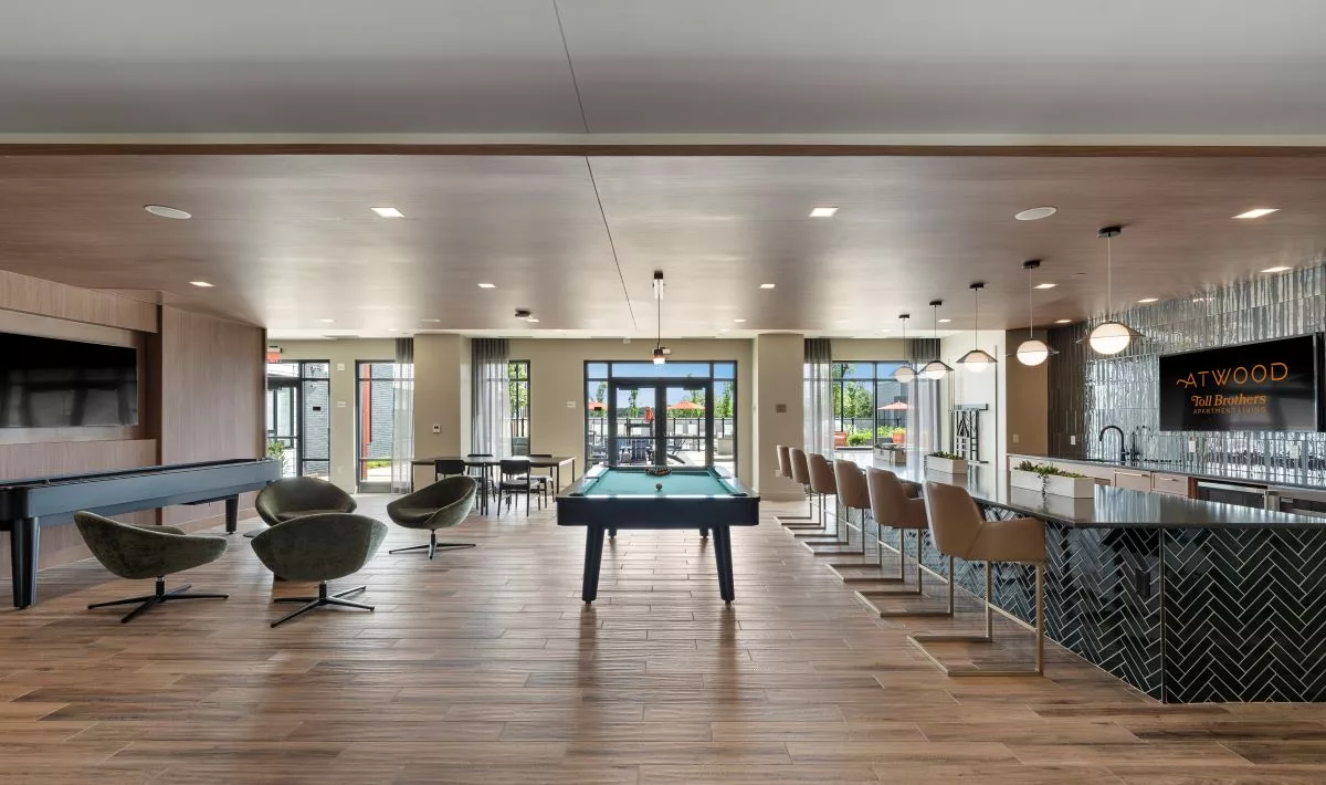 A lounge with low arm chairs, a pool table, and a bar with high chairs and hanging lights.