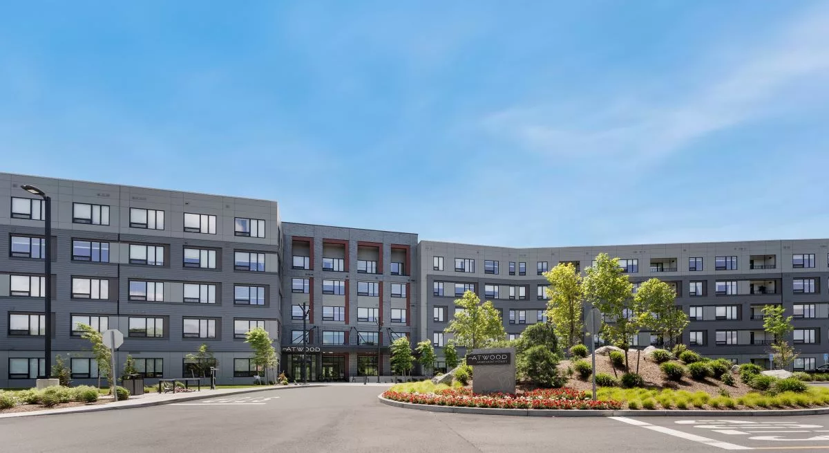 Exterior of an apartment building with gray exterior walls with red accents, and landscaping out from with a sign that says "Atwood".